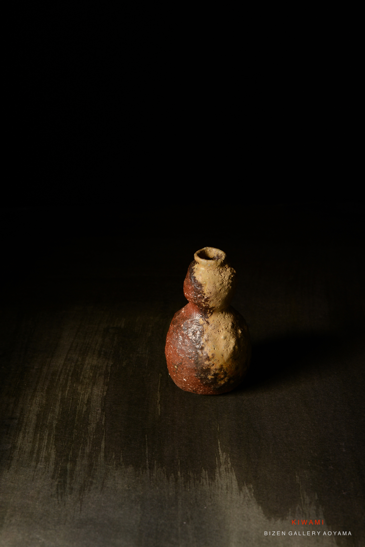 黒い背景に置かれた独特な形状の焼き物。色合いは赤、茶色、黄色で、表面は粗く仕上げられている。