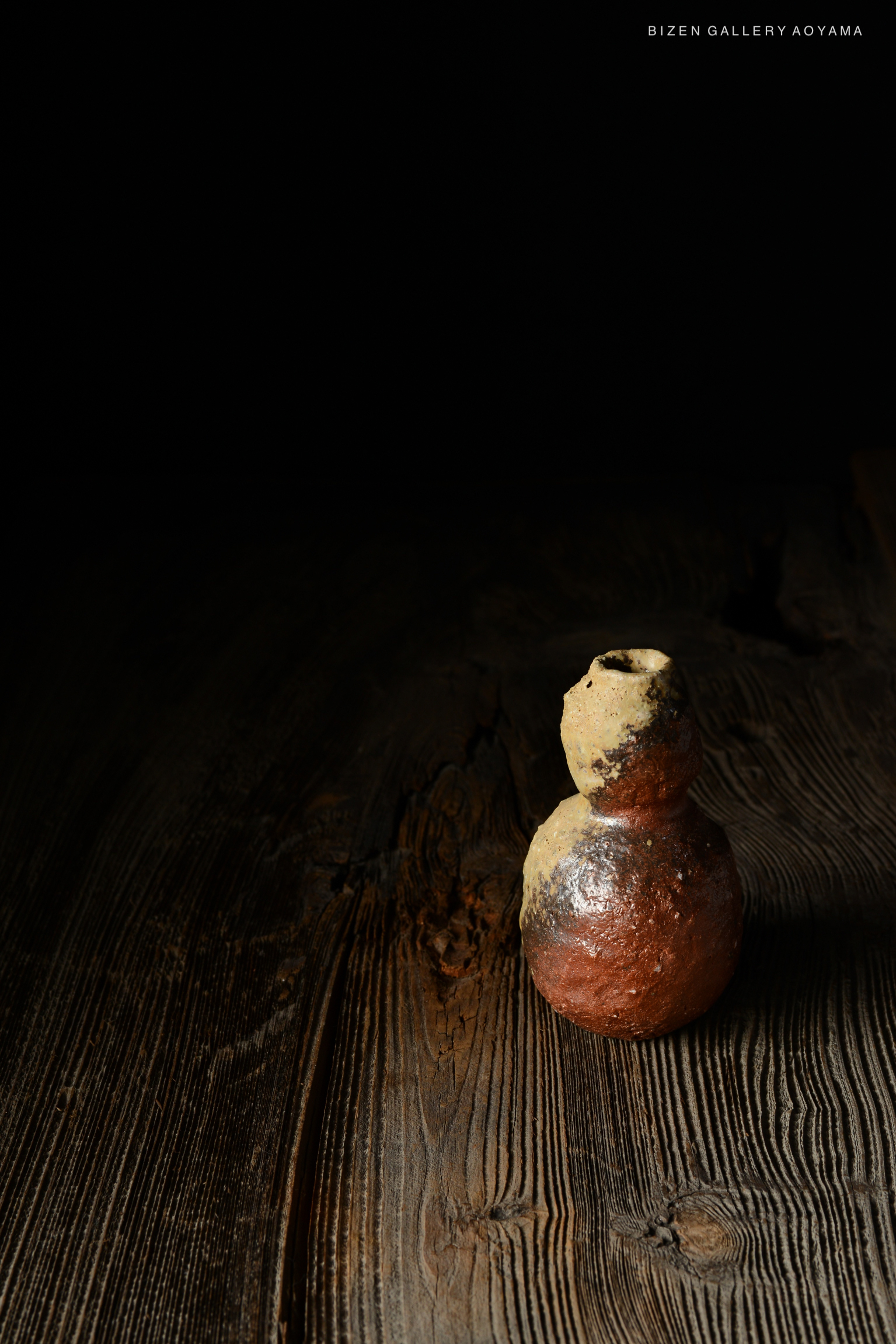 暗い背景の中に置かれた陶器の瓶。木製のテーブルの上に特徴的な形状で立っている。