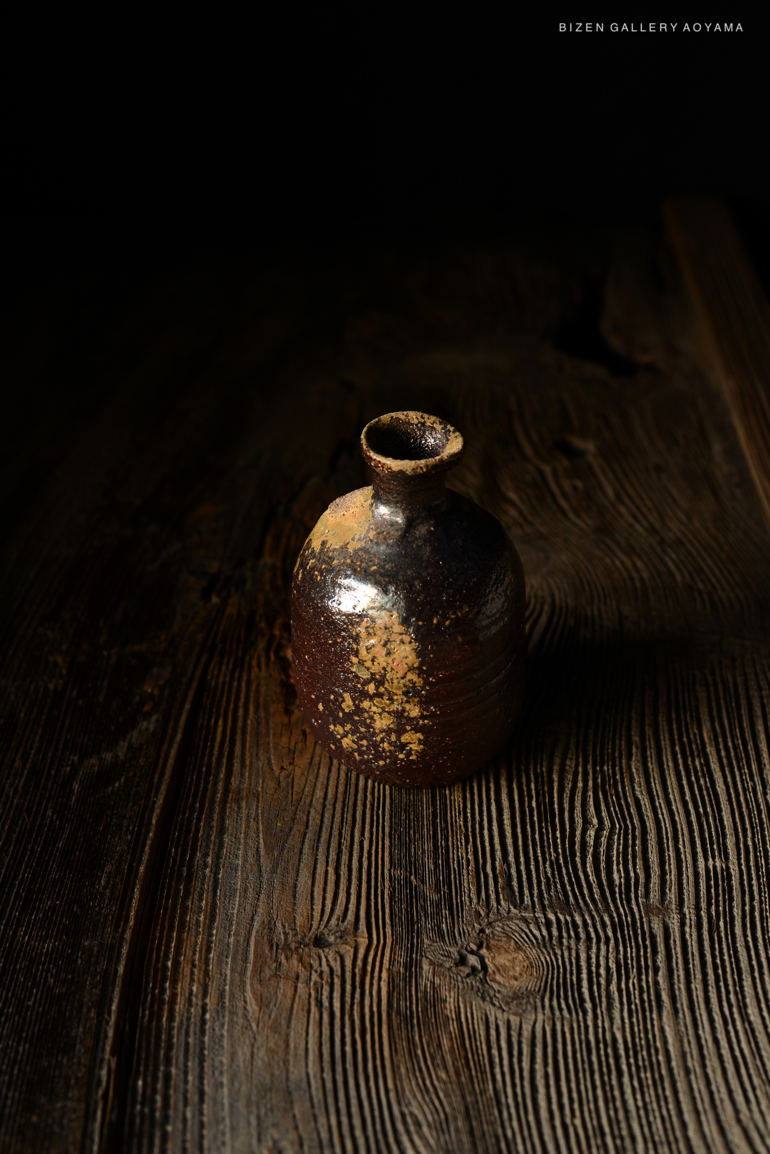 暗い背景の上に置かれた、独特なデザインの焼き物の瓶。木製のテーブルの上に撮影されている。