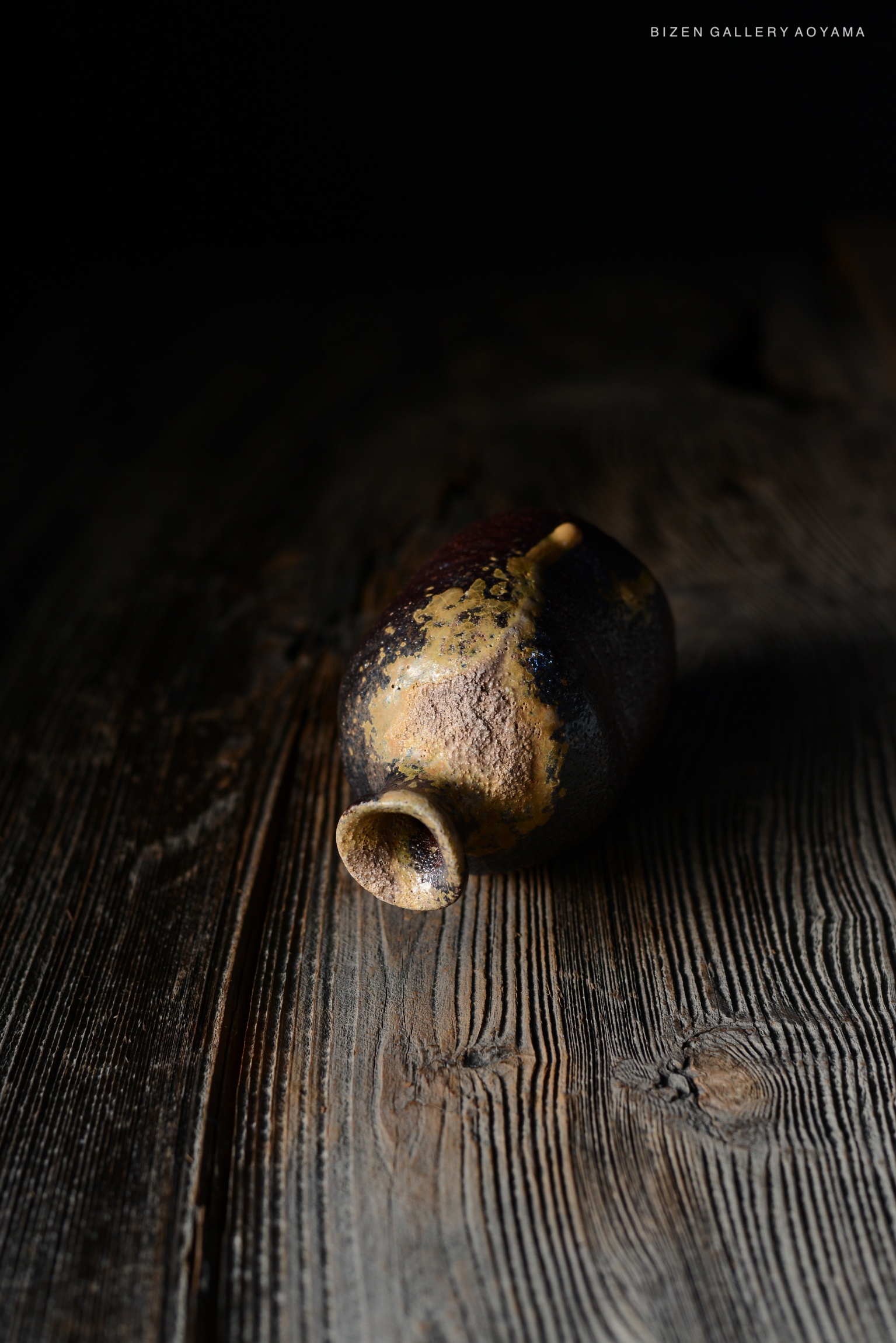 暗い背景の中に置かれた独特な形状の備前焼の壺が、木のテーブルの上にあります。