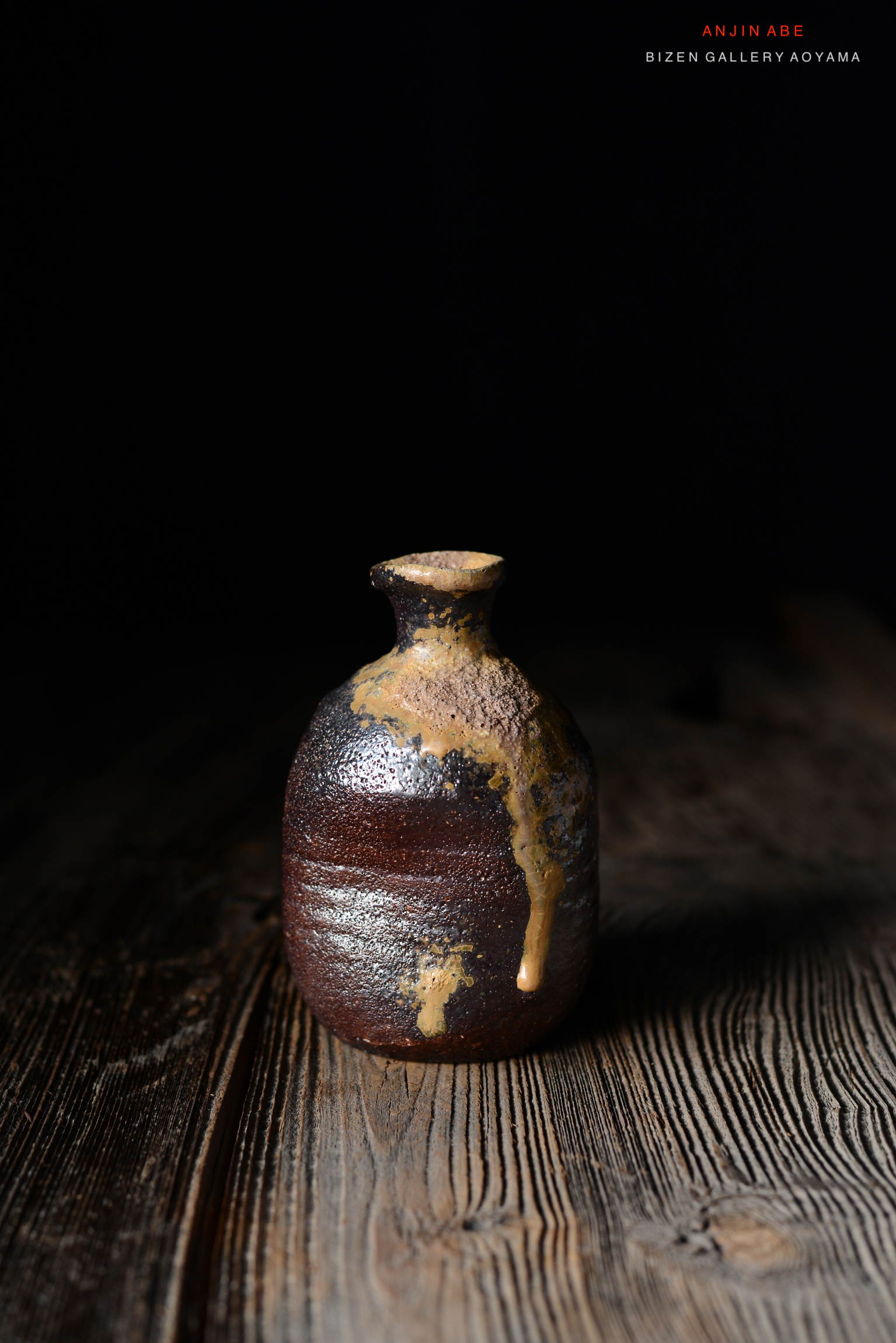 黒い背景の前に置かれた陶製の小さな瓶。瓶の表面には、茶色と金色のアクセントが施されている。木製のテーブルの上に置かれている。