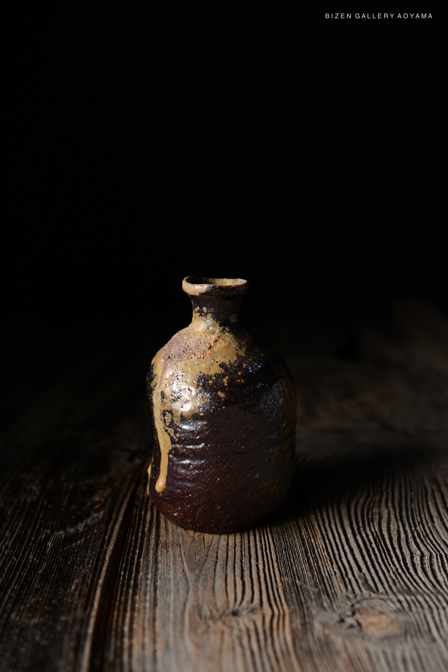 暗い背景の前に置かれた、独特の形状を持つ陶器の瓶。
