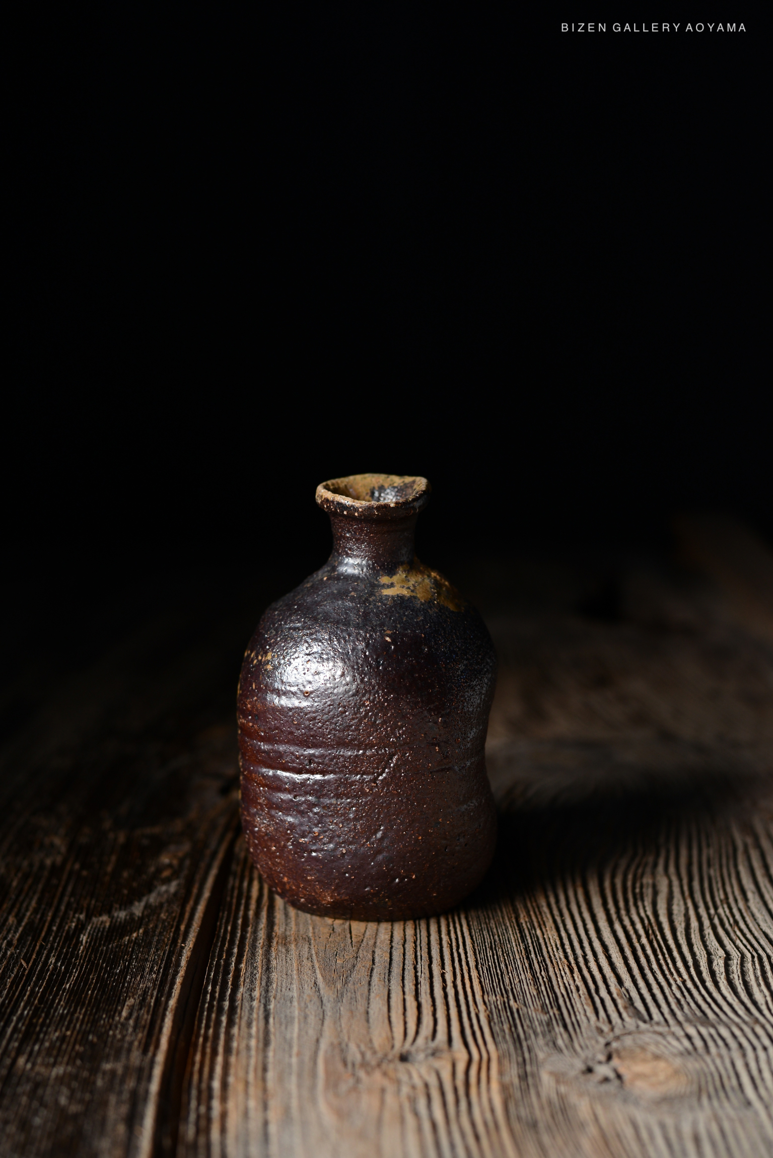 暗い背景の前に置かれた焼き物の瓶。木製のテーブルの上にあり、陶器の表面には光沢がある。