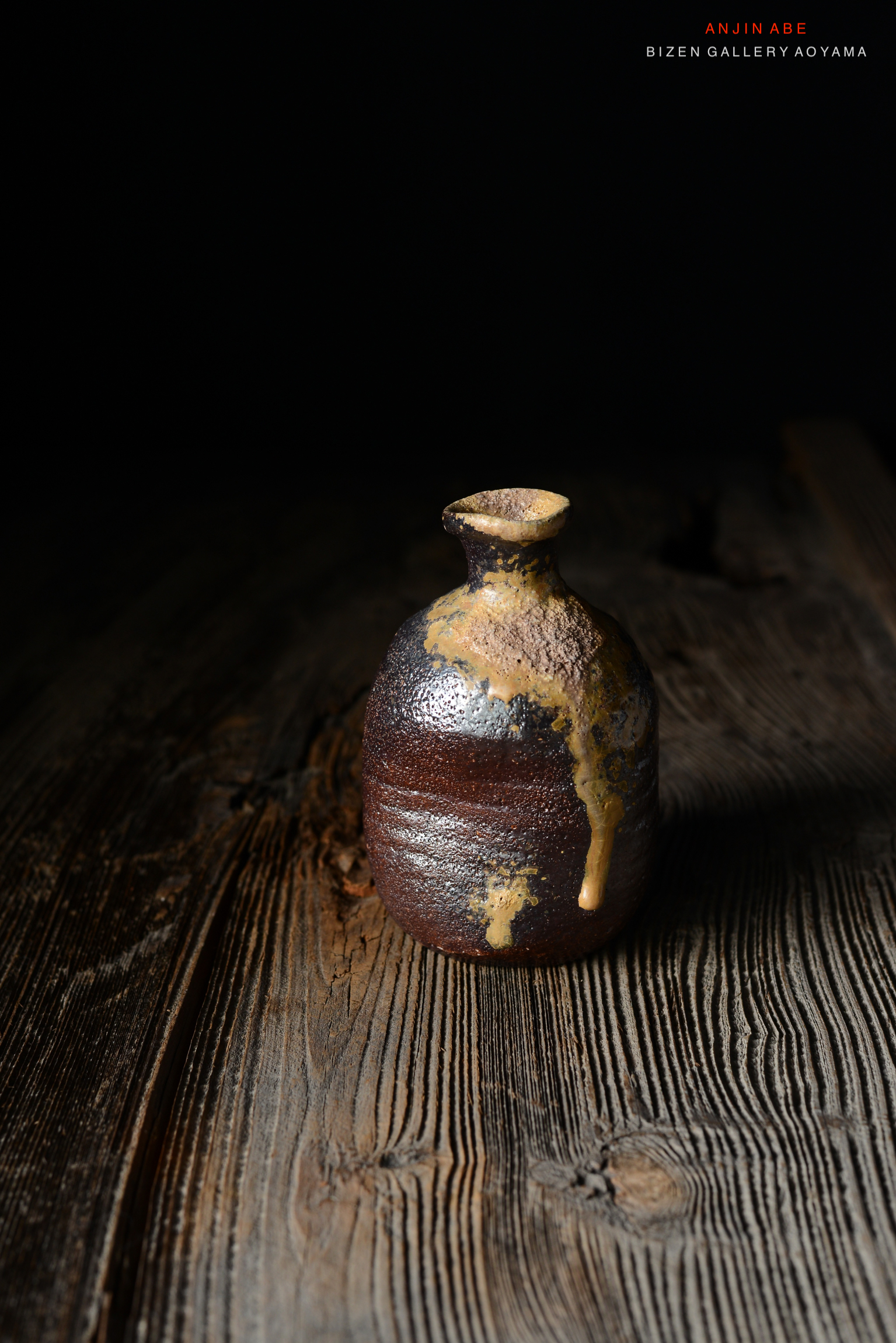 黒い背景の上に置かれた独特な形状の備前焼の陶器の壺。木のテーブルの上にあり、壺の表面には釉薬が滴り落ちている。