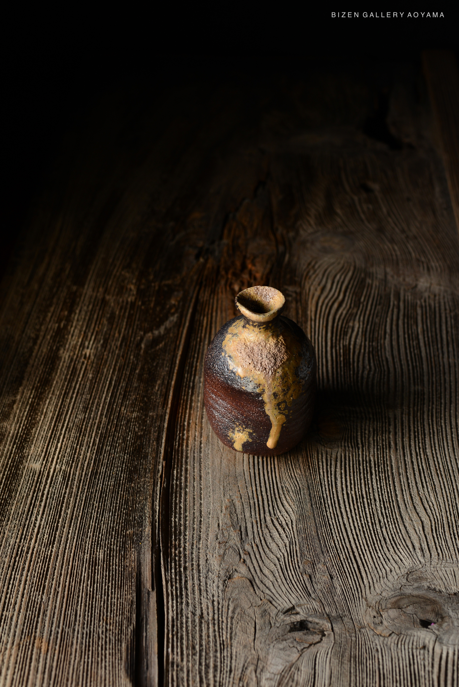 古い木のテーブルの上に置かれたビゼン焼きの陶器。暗い背景で陶器の質感と色合いが際立つ。