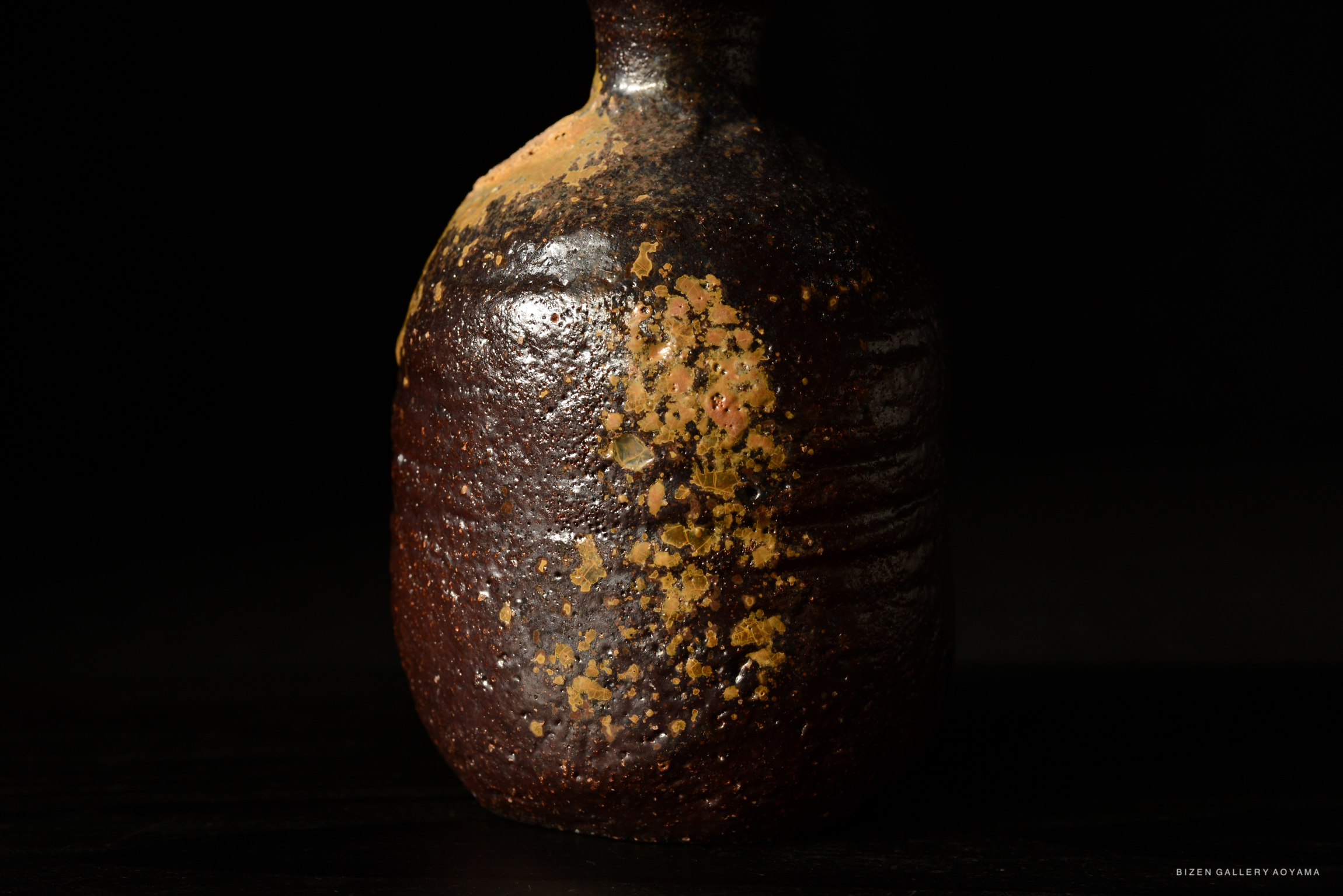 黒い背景に置かれた陶器の壺。表面は、茶色と金色の斑点が特徴的。