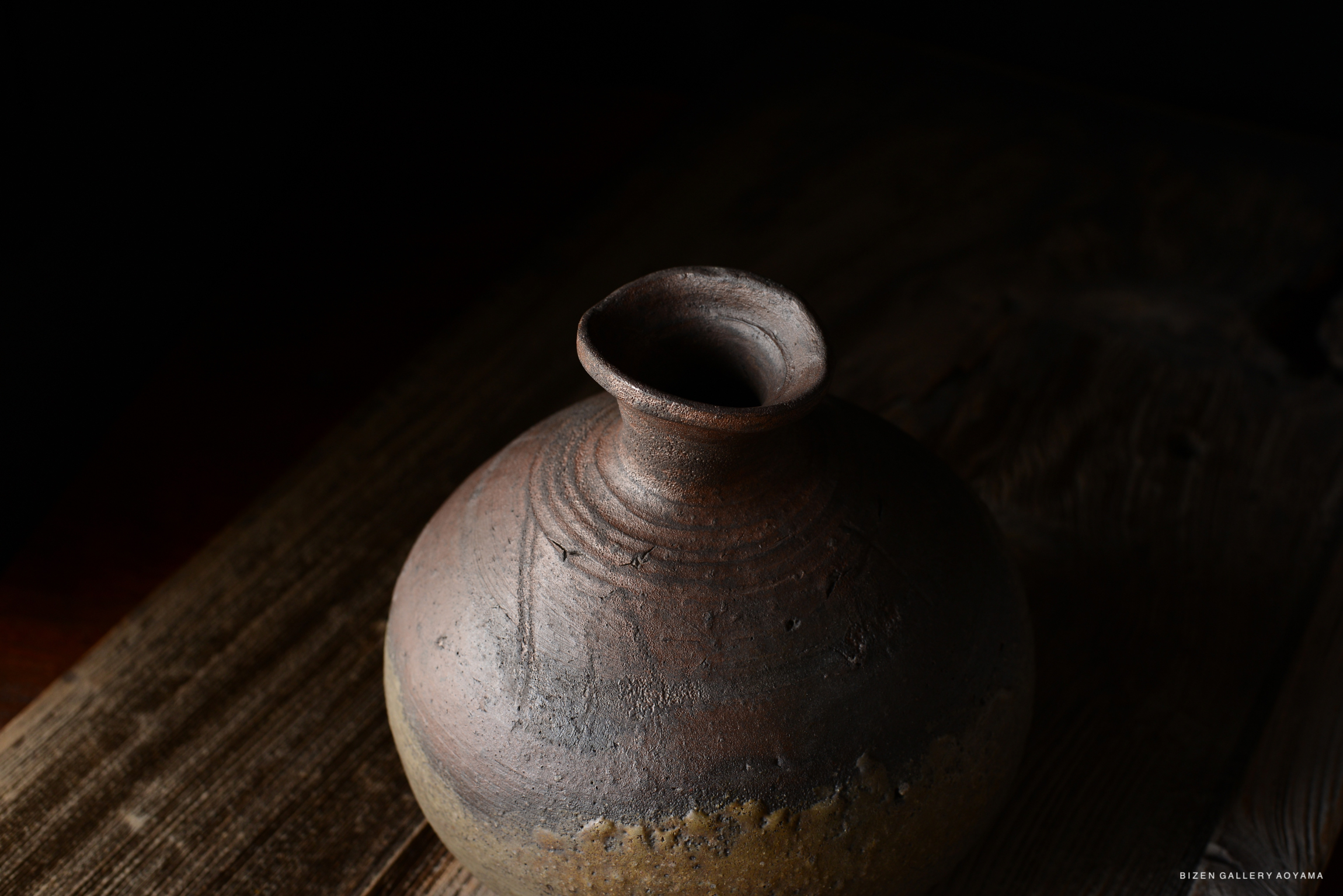 Close-up of a round, rustic clay pot with a narrow neck, resting on a wooden surface.
