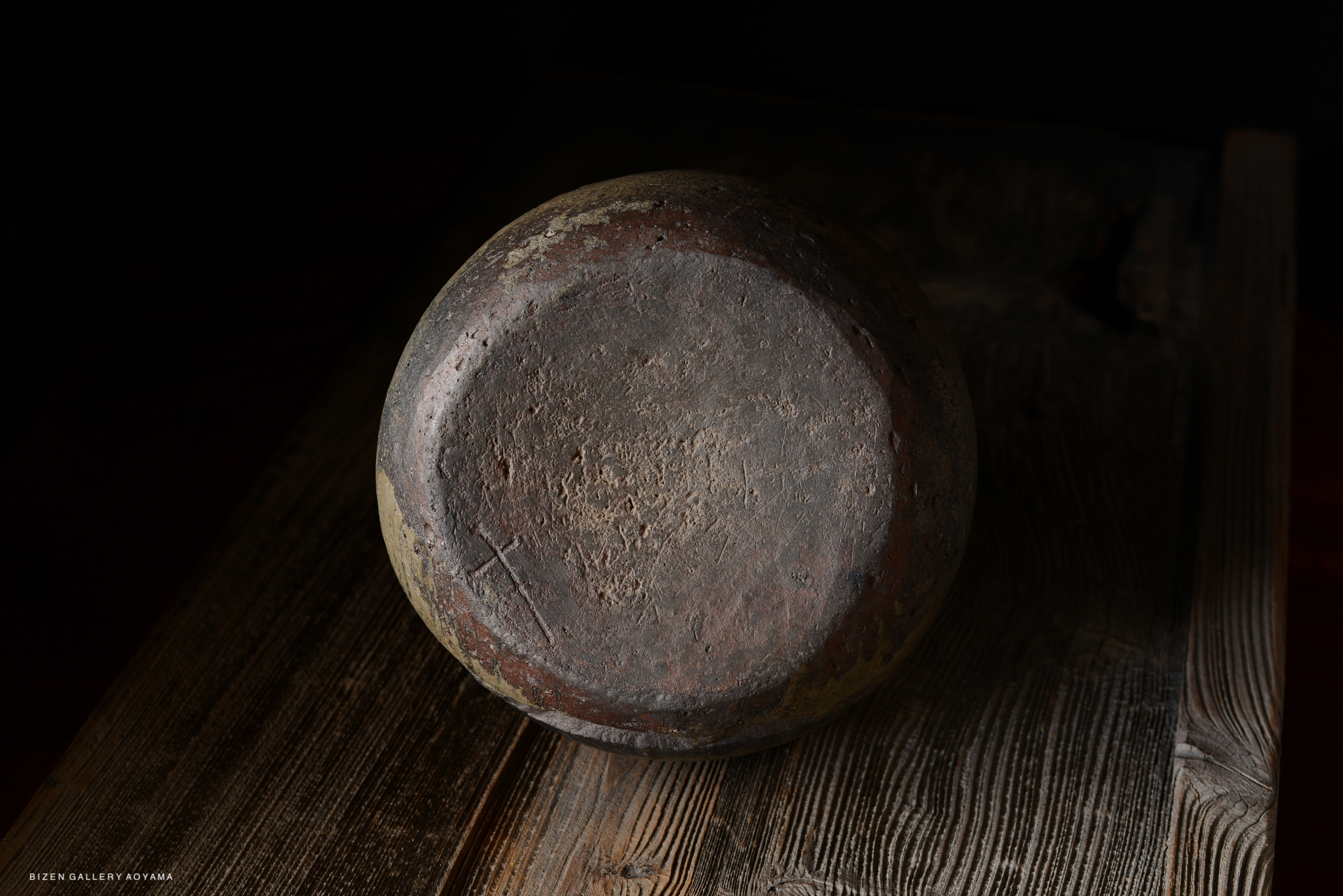 A round, rustic pottery bowl with a textured surface placed on a wooden table, shown from above.