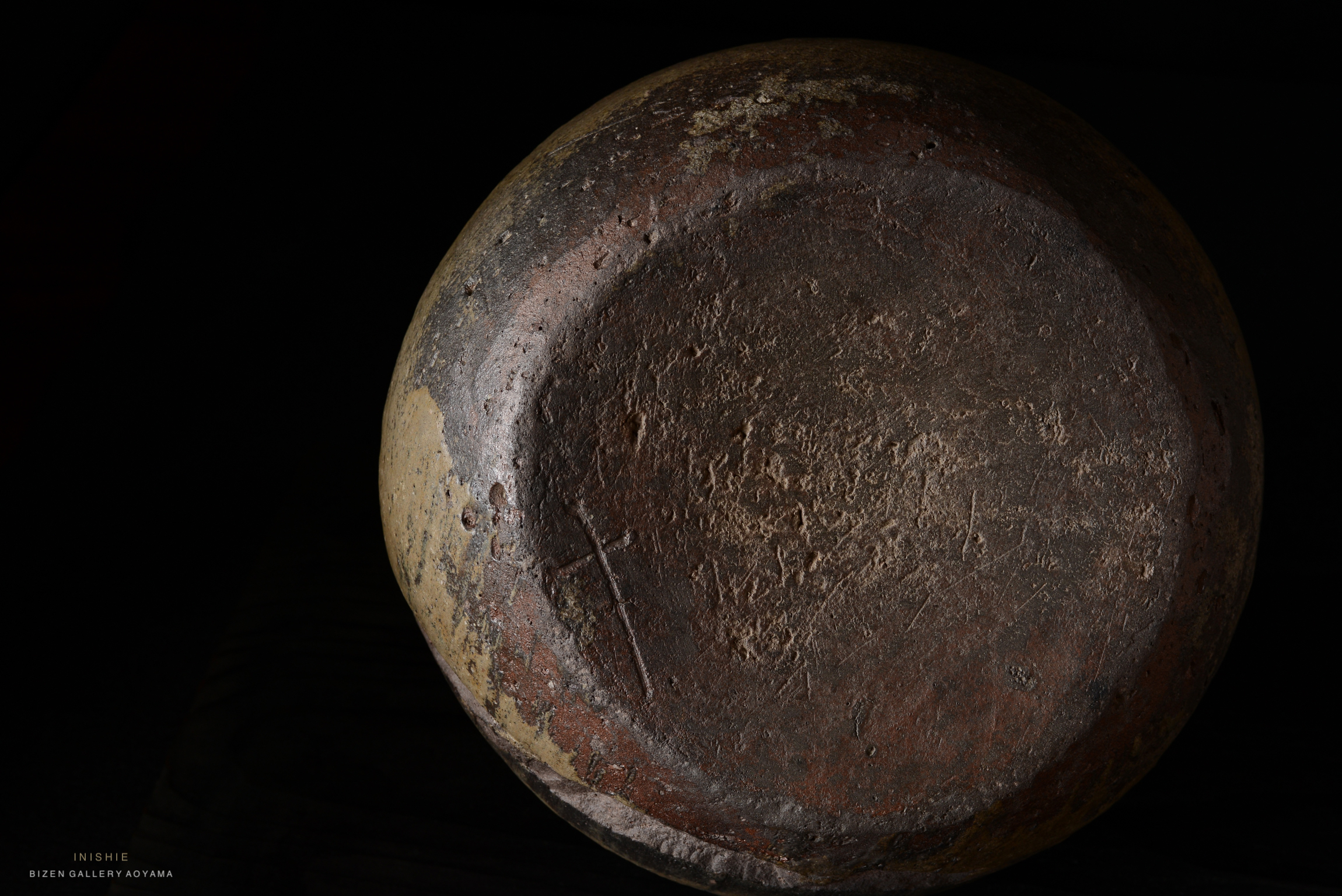 Close-up view of a textured, circular, antique pottery piece highlighting its rough surface and earthy colors.