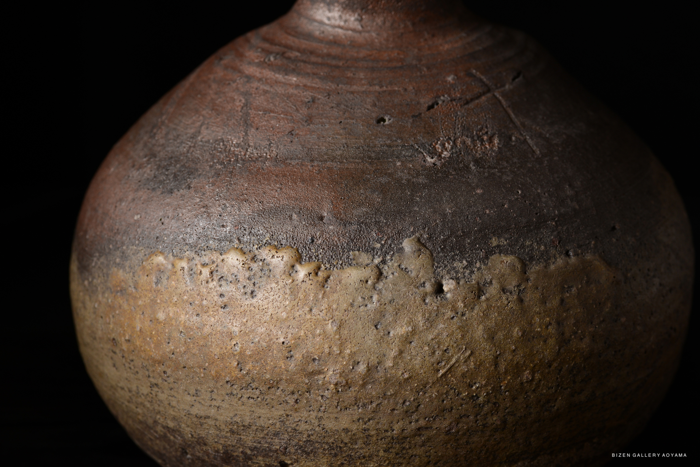 Close-up of an aged, textured ceramic vessel with a brown and cream gradient, featuring distinctive surface markings and imperfections against a dark background.