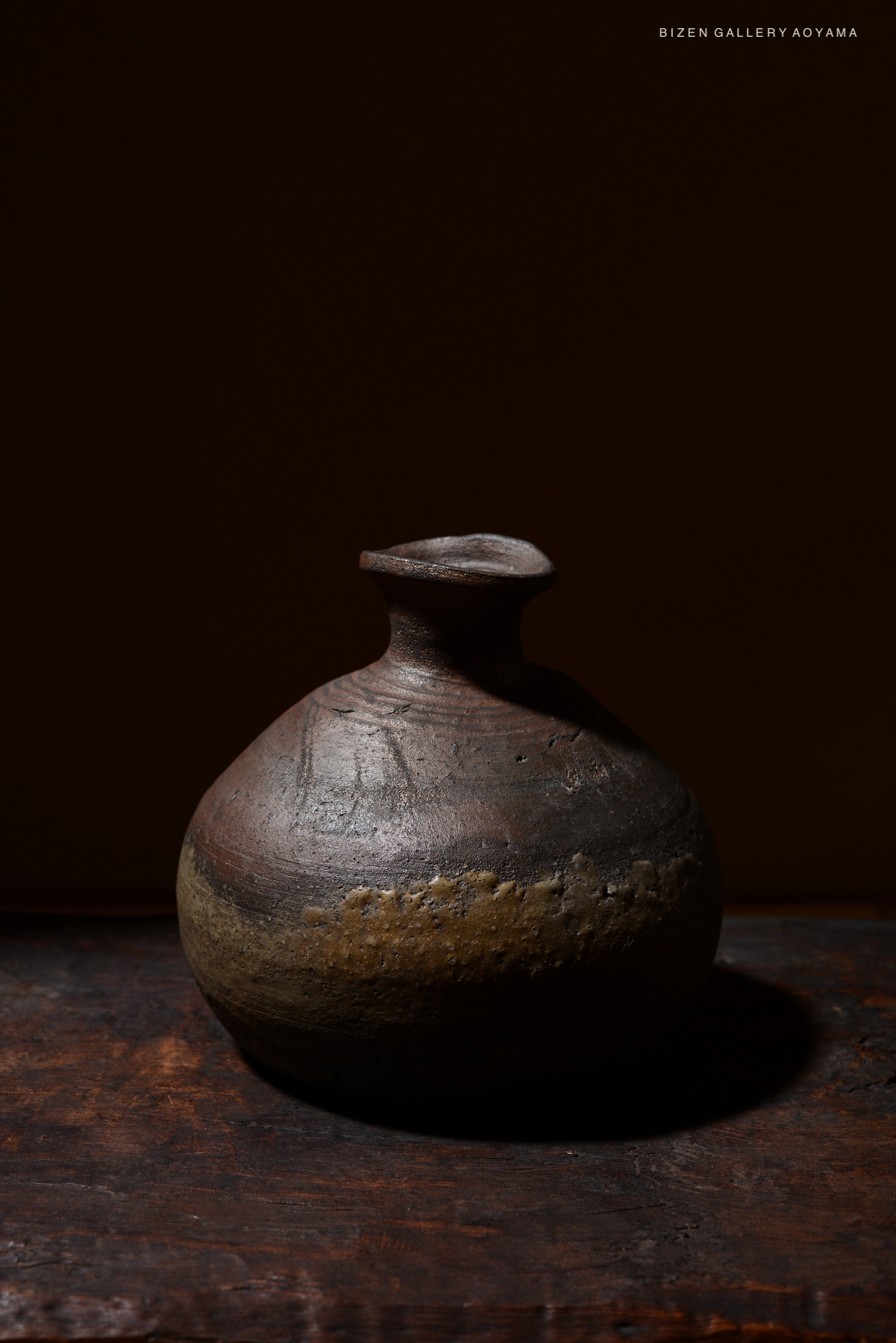 A traditional Bizen pottery Tokkuri, characterized by its rounded body and narrow mouth, displayed against a dark background, showcasing its earthy tones and unique texture.