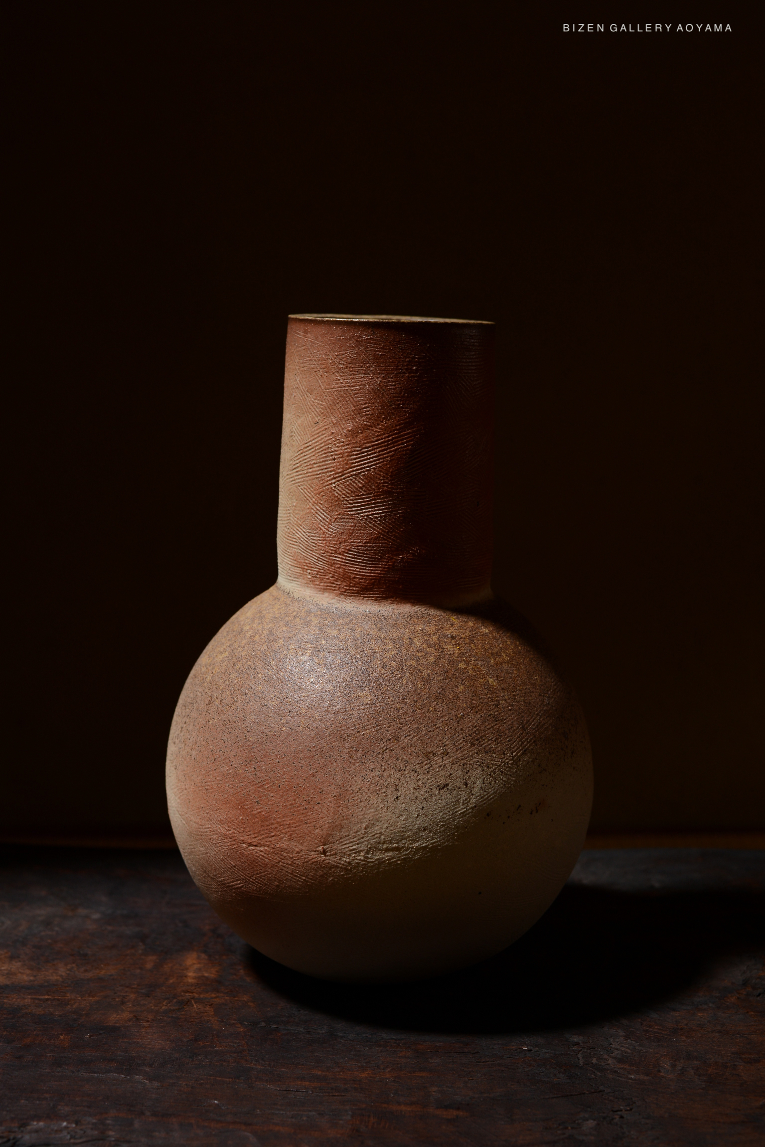 A close-up view of a traditional Bizen pottery vase with a rounded body and a narrow neck, showcasing earthy colors and textures against a dark background.