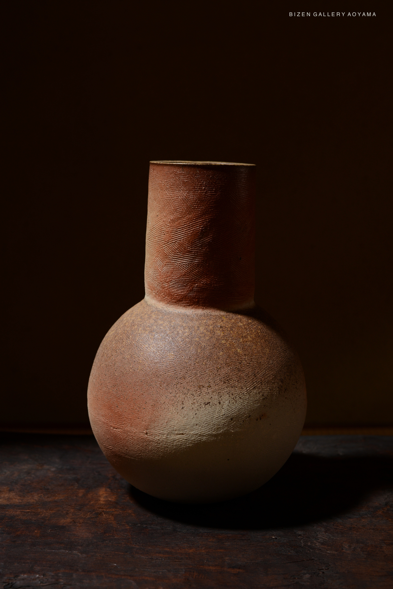 A beautifully crafted Bizen pottery vase with a round base and a narrow neck, featuring earthy tones of brown and beige against a dark background.