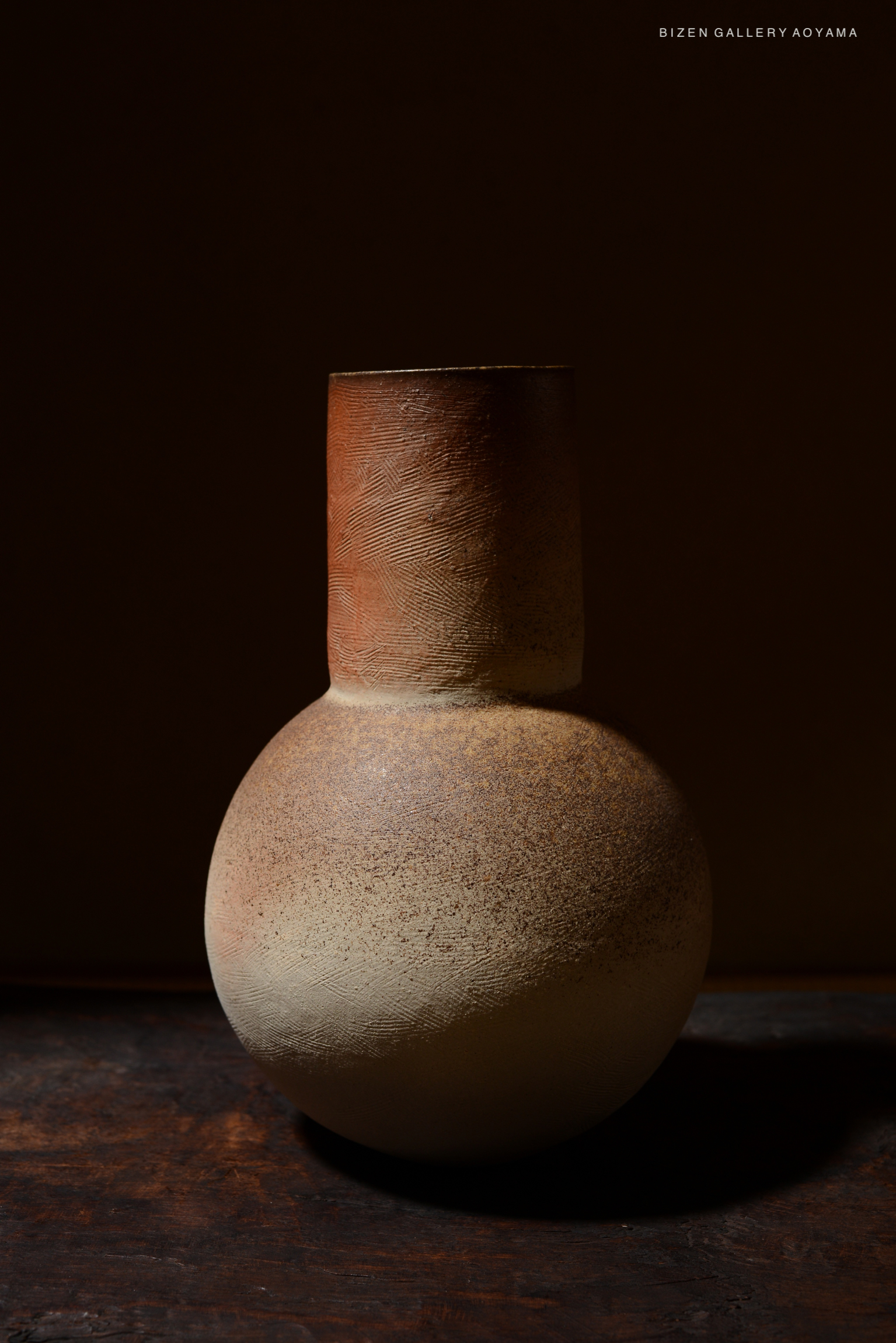 A close-up image of a ceramic vase with a round base and a cylindrical neck, featuring earthy tones and textured surfaces, set against a dark background.
