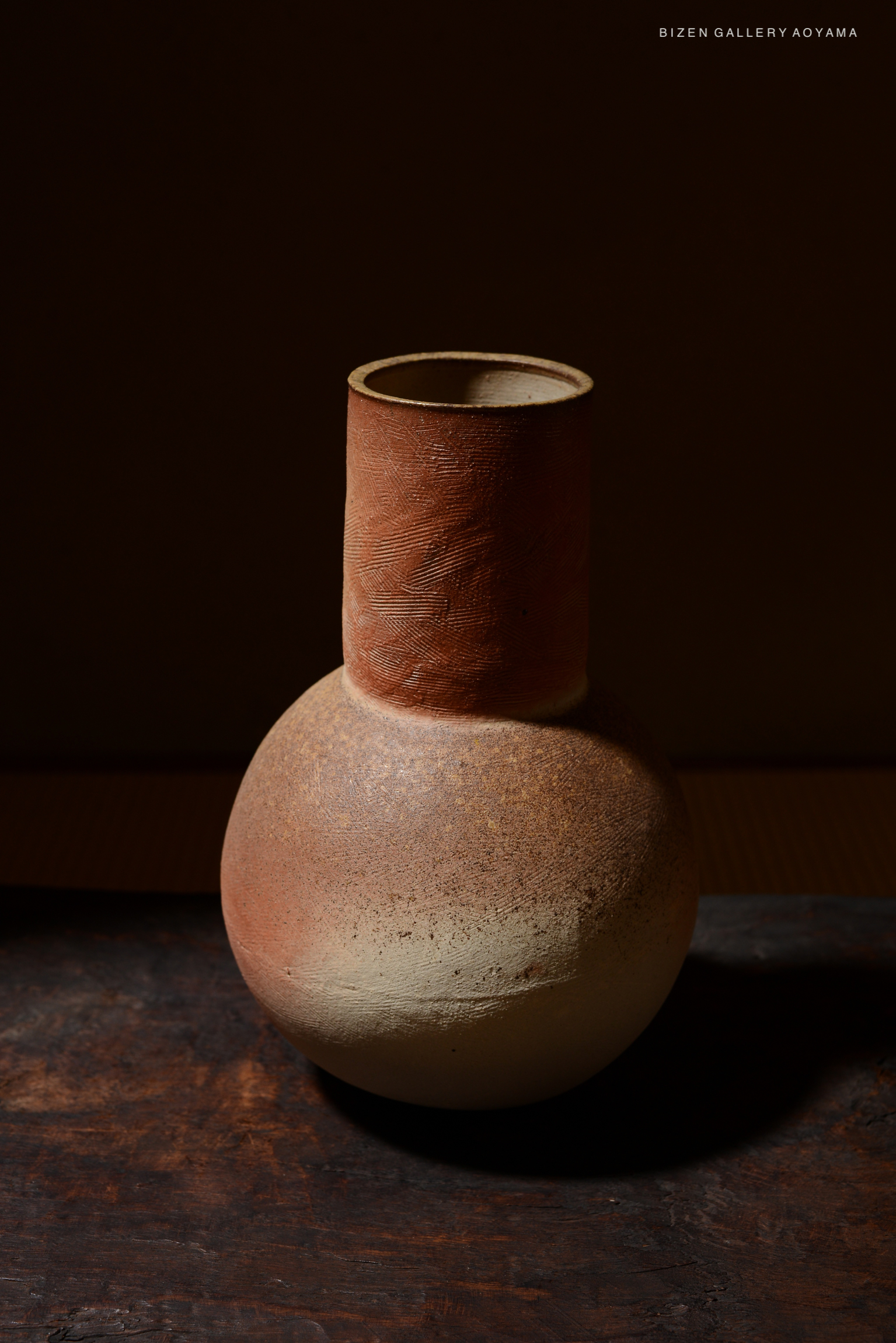 A handcrafted ceramic vase with a spherical base and a tall, narrow neck, featuring earthy tones of brown and beige, set against a dark background.