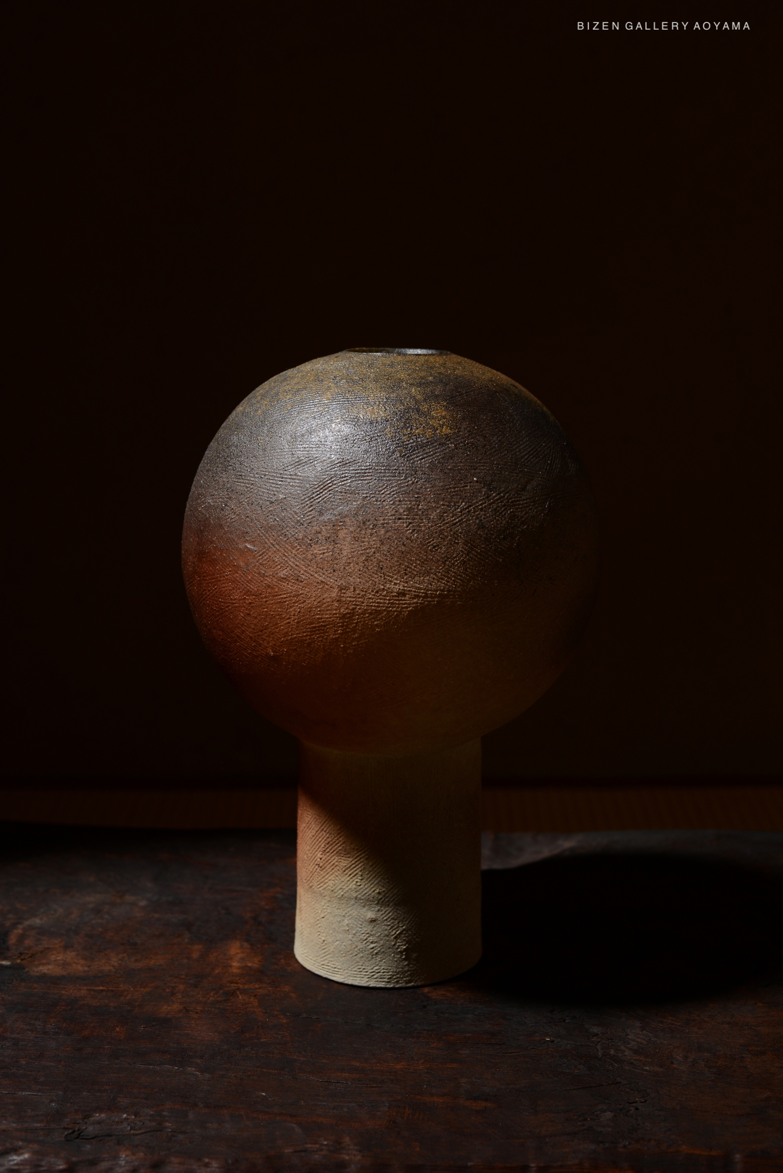 A round ceramic vase with a spherical top and cylindrical base, set against a dark background.