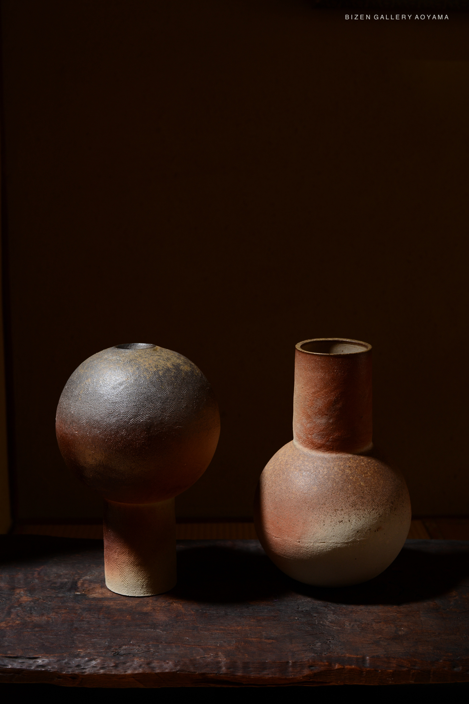 Two ceramic vases displayed on a wooden surface, featuring a spherical vase on the left and a rounded, necked vase on the right, both showcasing earthy tones.