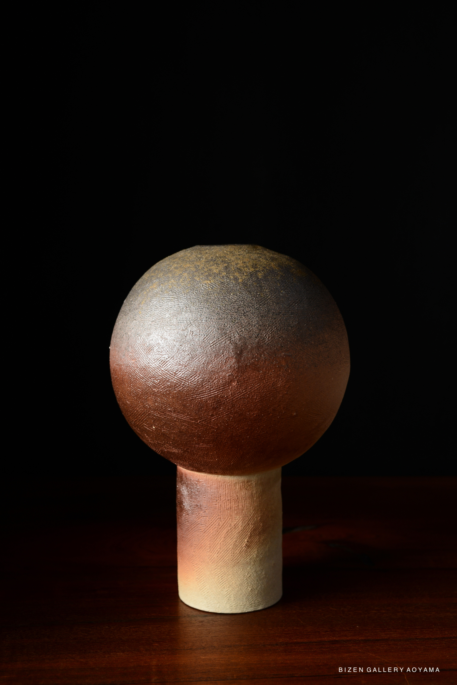 Ceramic lamp with a spherical top and cylindrical base, featuring earthy tones and textured surface, set against a dark background.