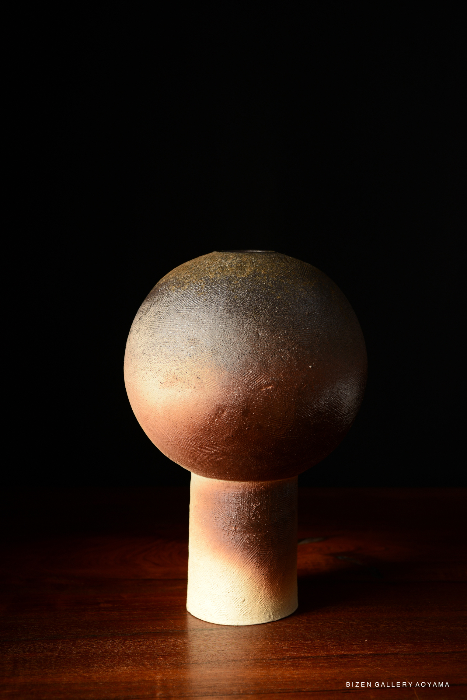 A decorative ceramic vase with a spherical top and a cylindrical base, showcasing a gradient of earthy tones against a dark background.