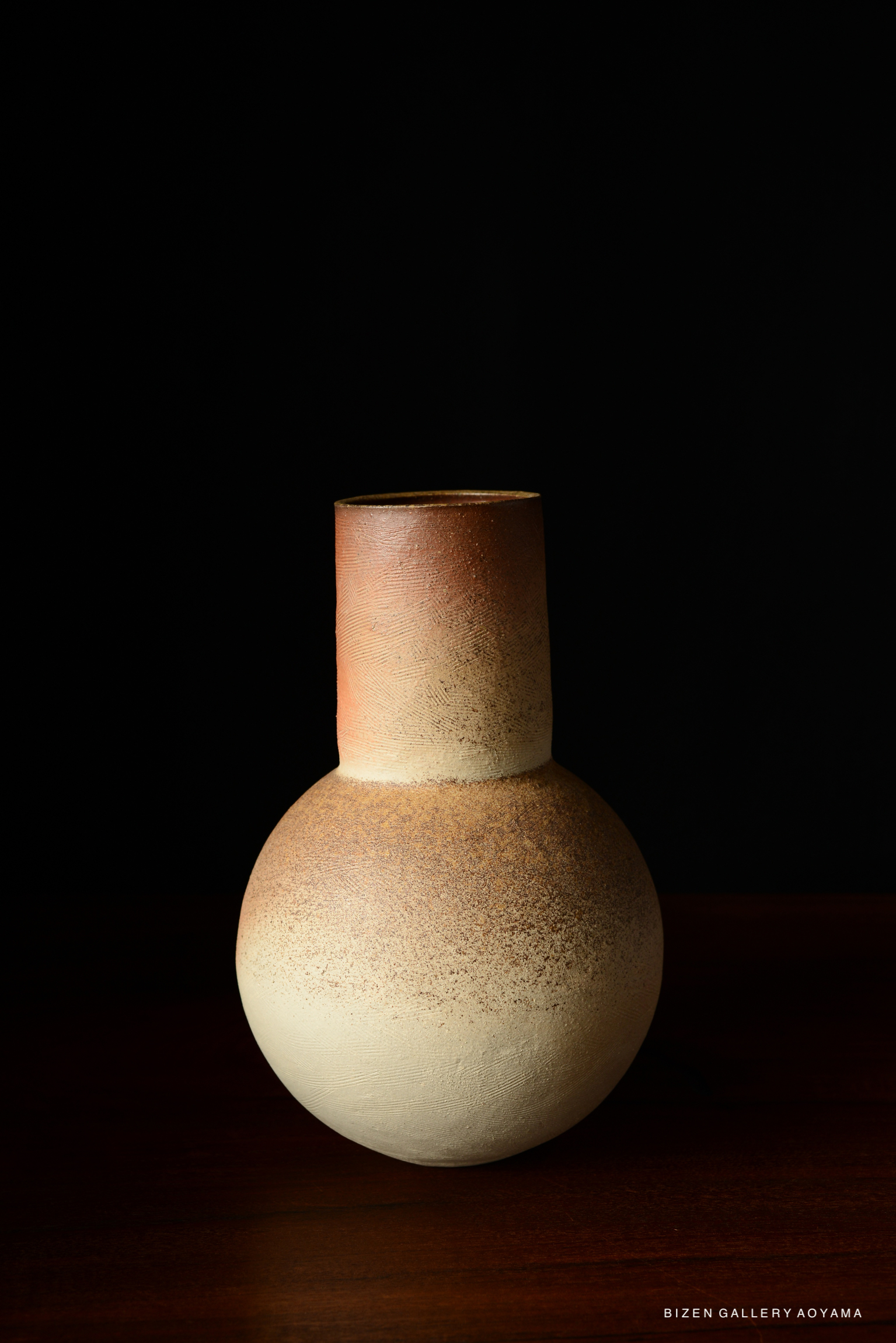 A ceramic vase with a round body and a tall neck, featuring a gradient of brown and cream colors against a dark background.