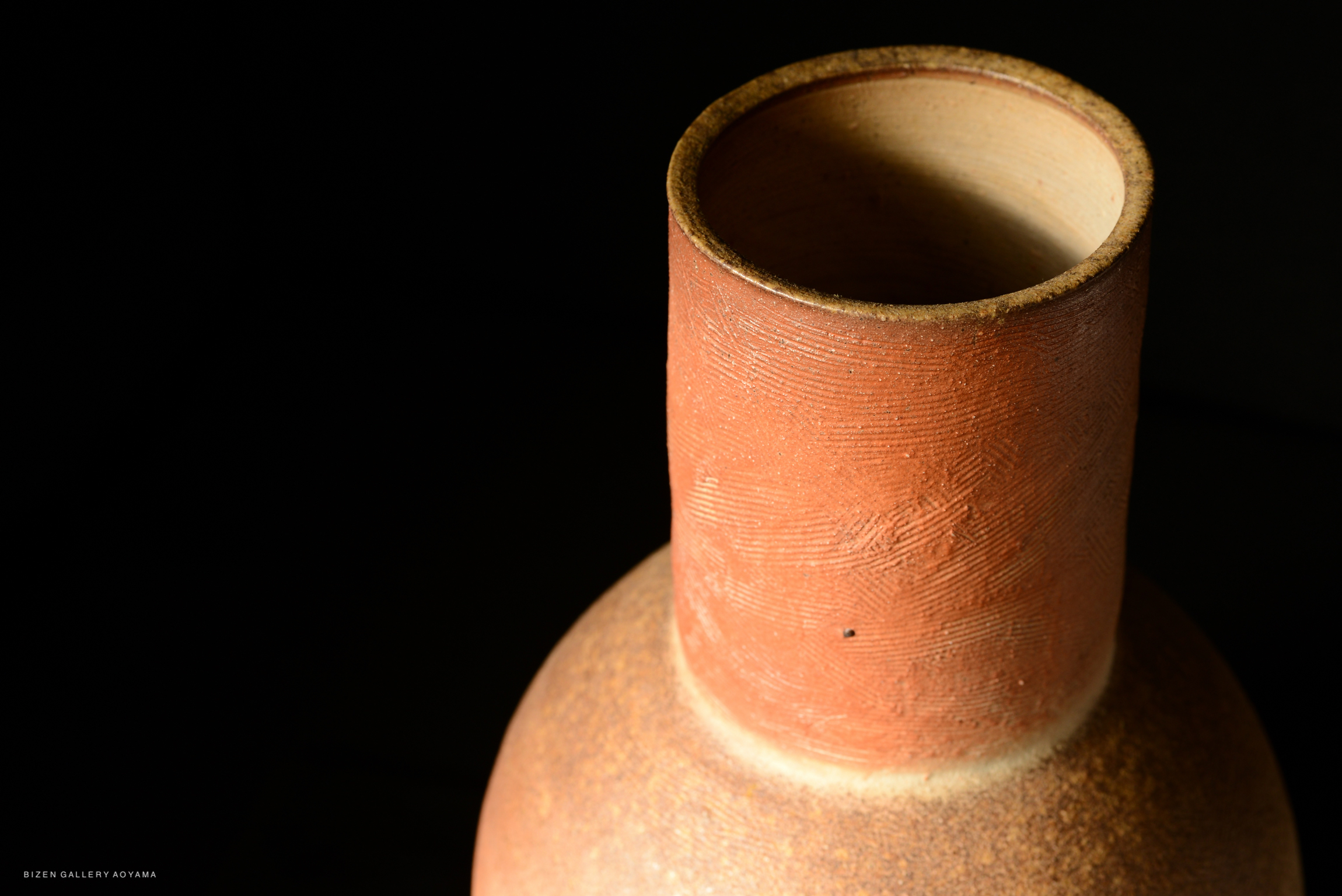 Close-up of a traditional Japanese long-necked vase, showcasing its textured surface and earthy tones against a dark background.