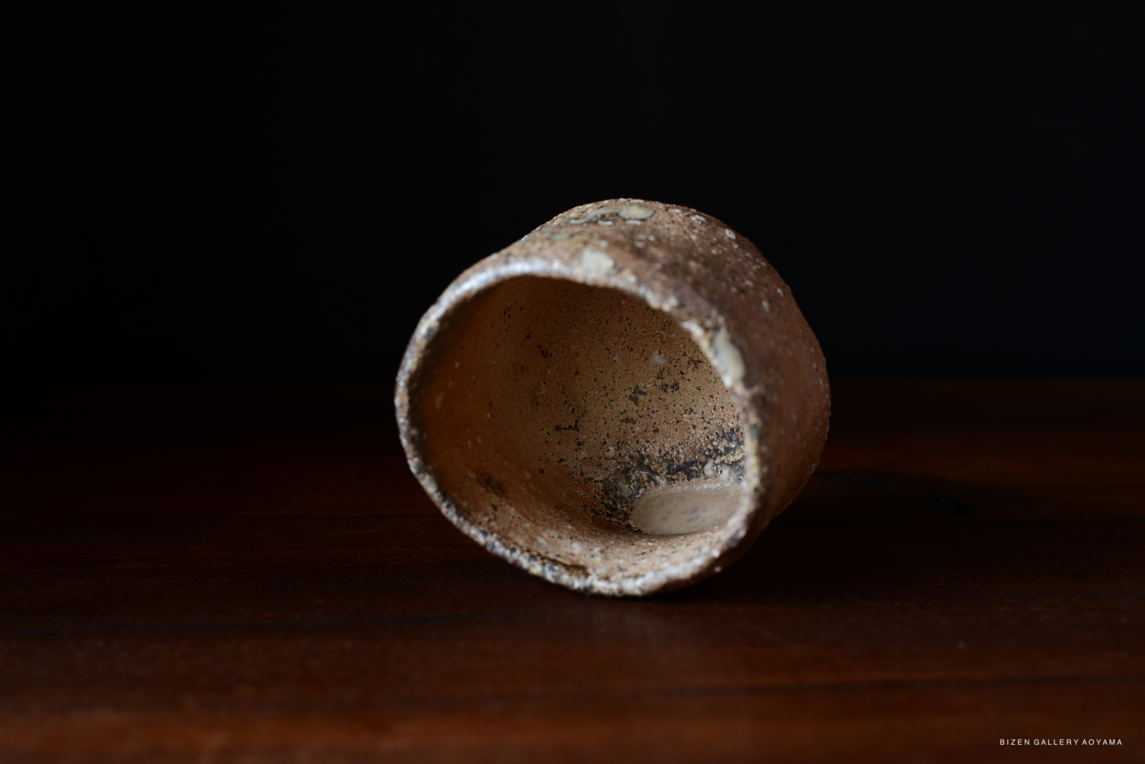壺の底が見える焼き物の写真。黒い背景に対して、木のテーブルに置かれた陶器の器。
