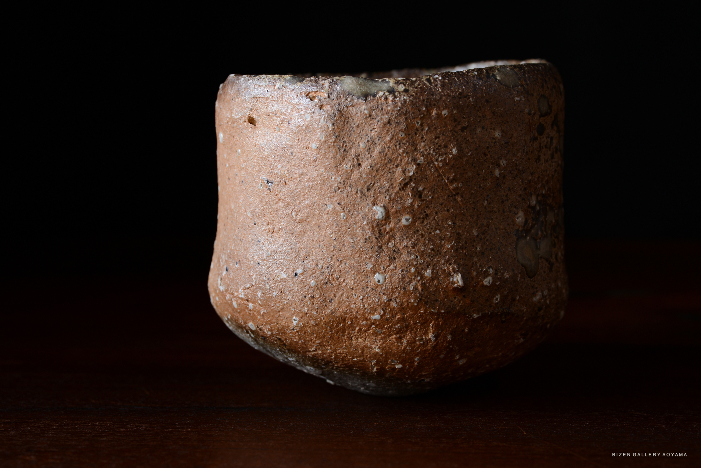 黒い背景に置かれた焼き物の陶器の茶碗。表面はざらざらしており、茶色と灰色の色合いが見える。
