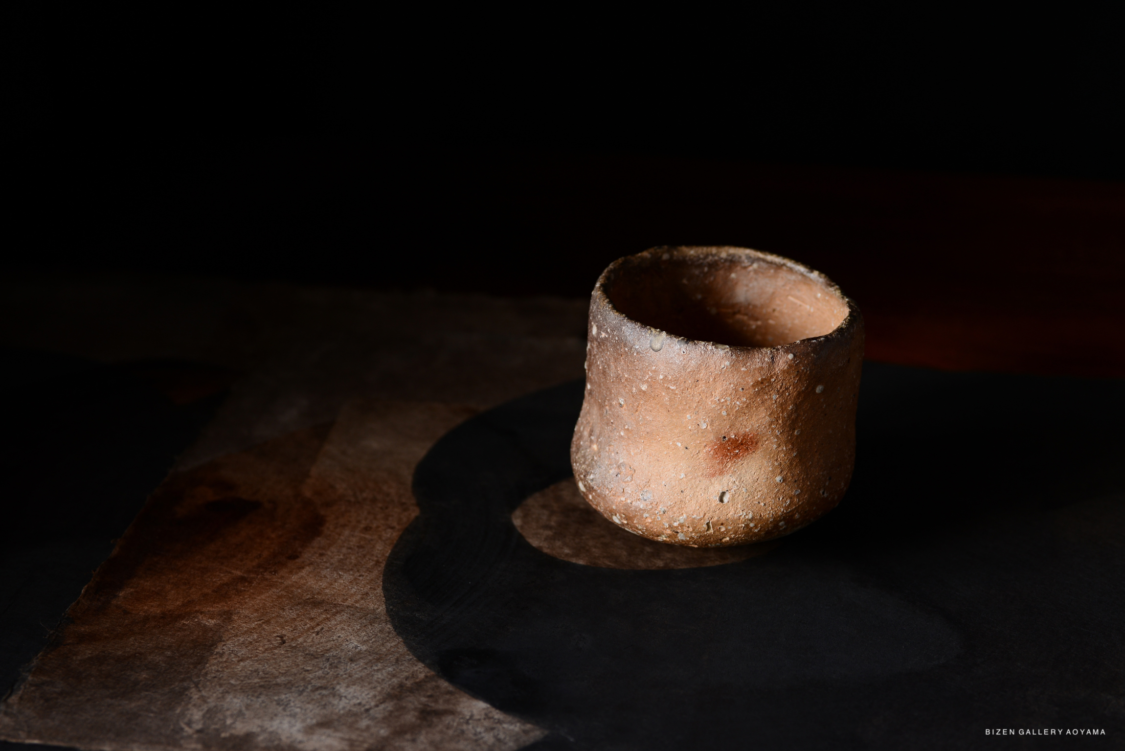 黒い背景に置かれた素焼きの陶器の器。部分的に光が当たっている。
