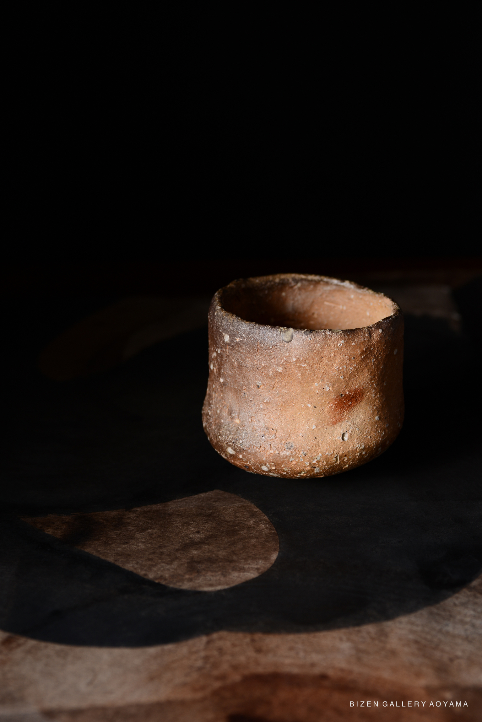 黒い背景の前に置かれた、素朴な質感の陶器のカップの画像。