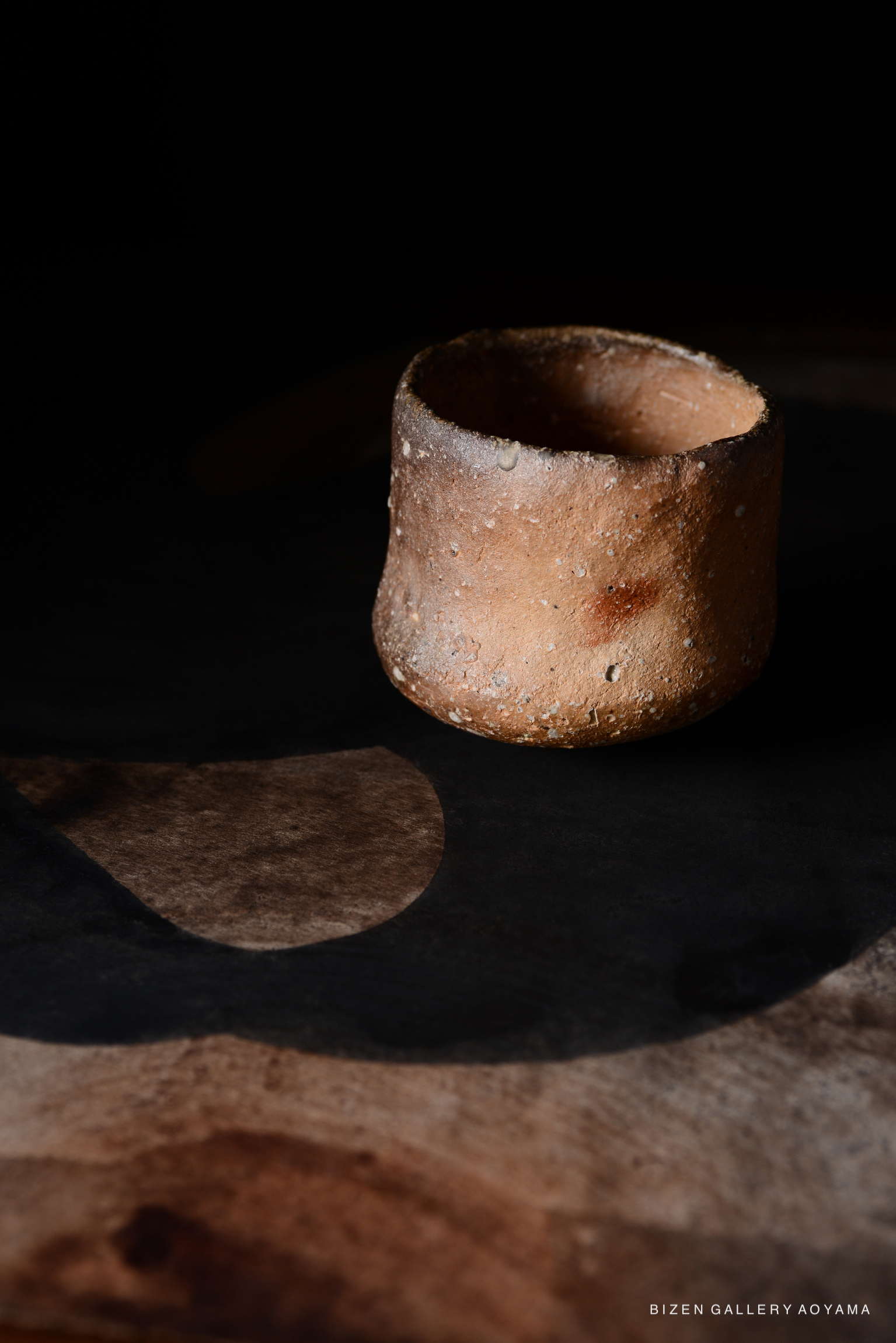 暗い背景の上に置かれた陶器の器。柔らかい光が当たり、周囲に影を落としている。