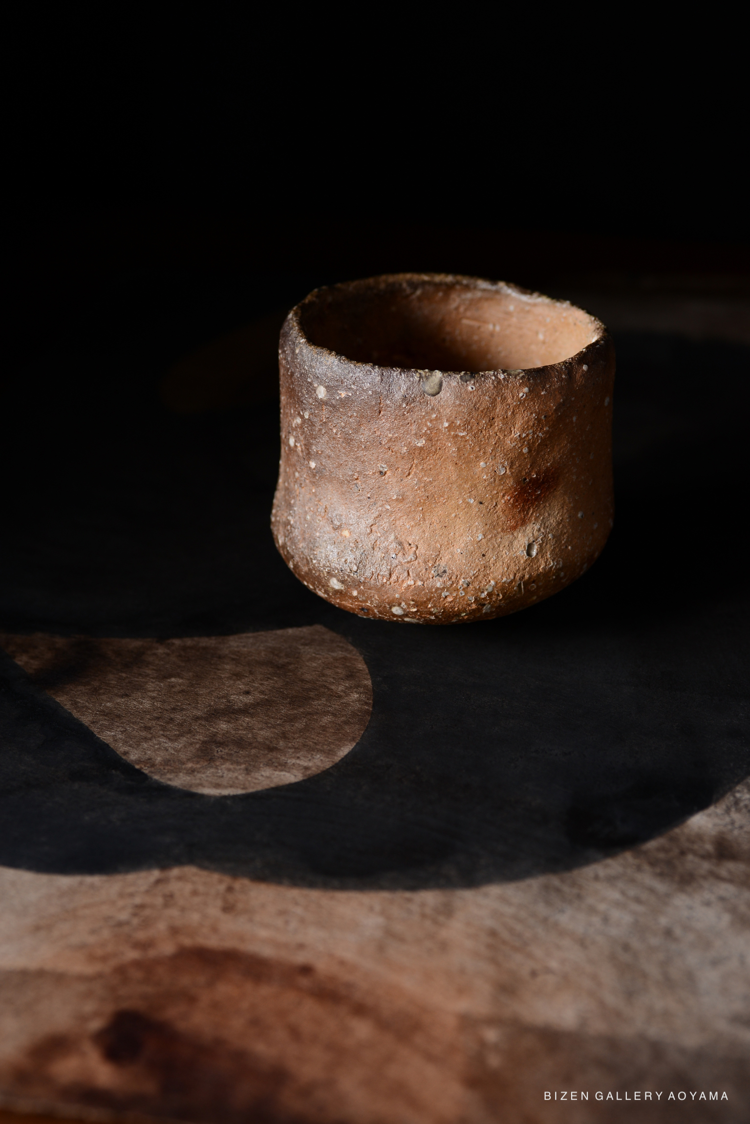 黒背景の上に置かれた、焼き物の質感を持つ茶色の陶器の器