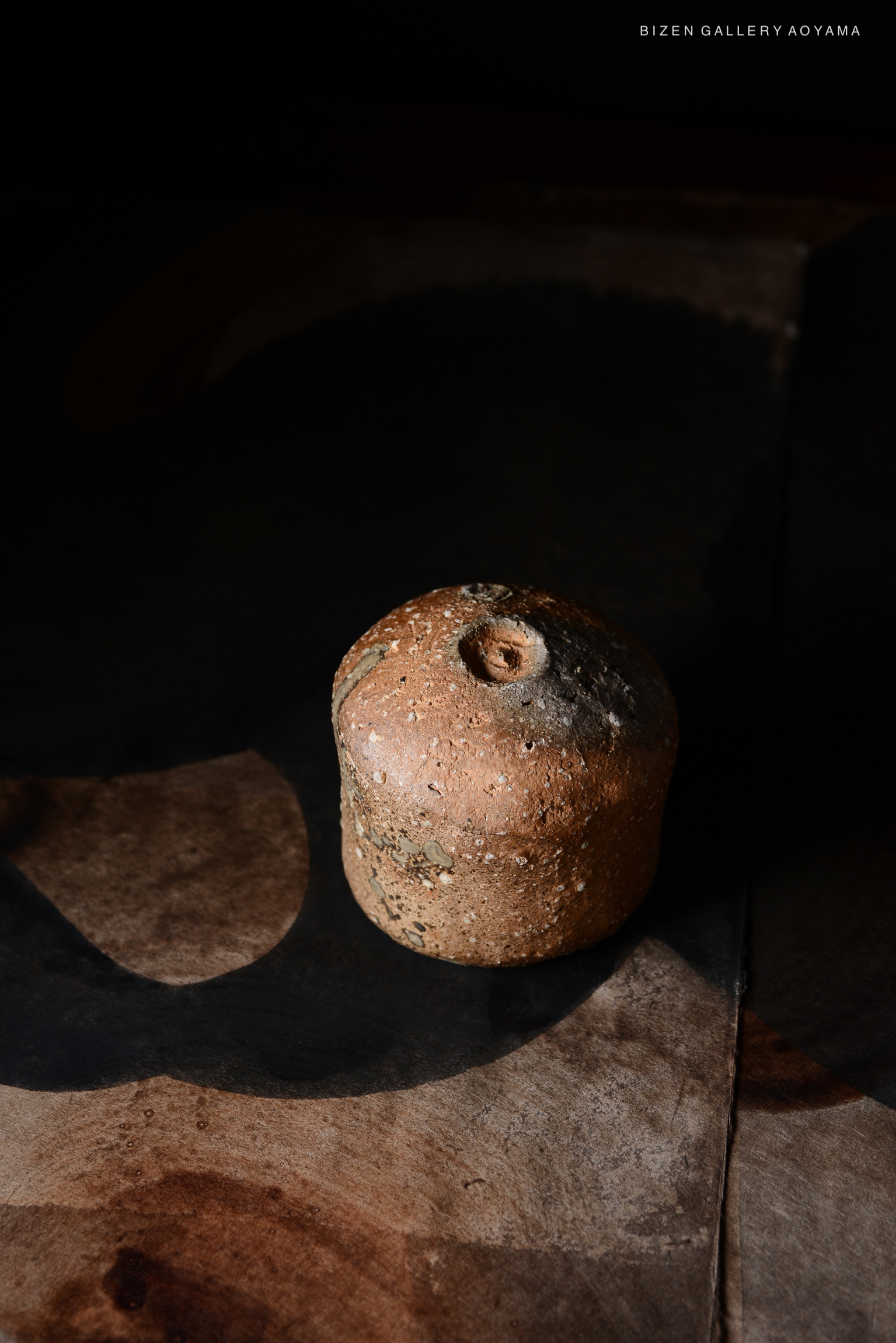 土の質感と丸みを帯びた形状を持つ備前焼の壺が暗い背景の上に置かれている