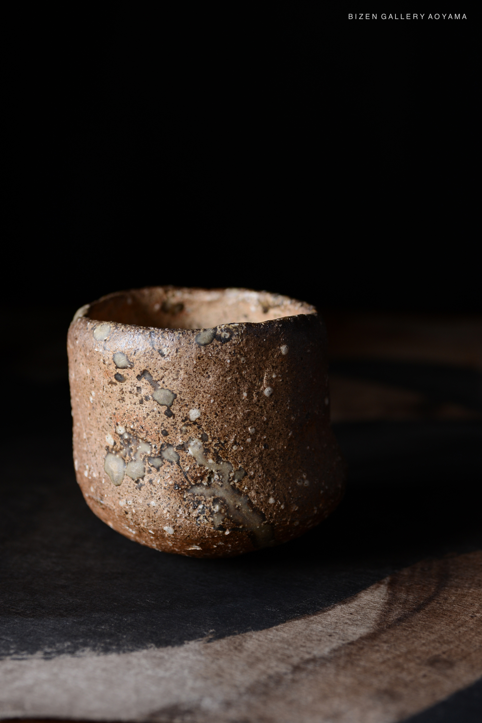 ビゼン焼きの土製の器が、暗い背景の上に置かれています。表面には独特な模様とテクスチャーがあります。