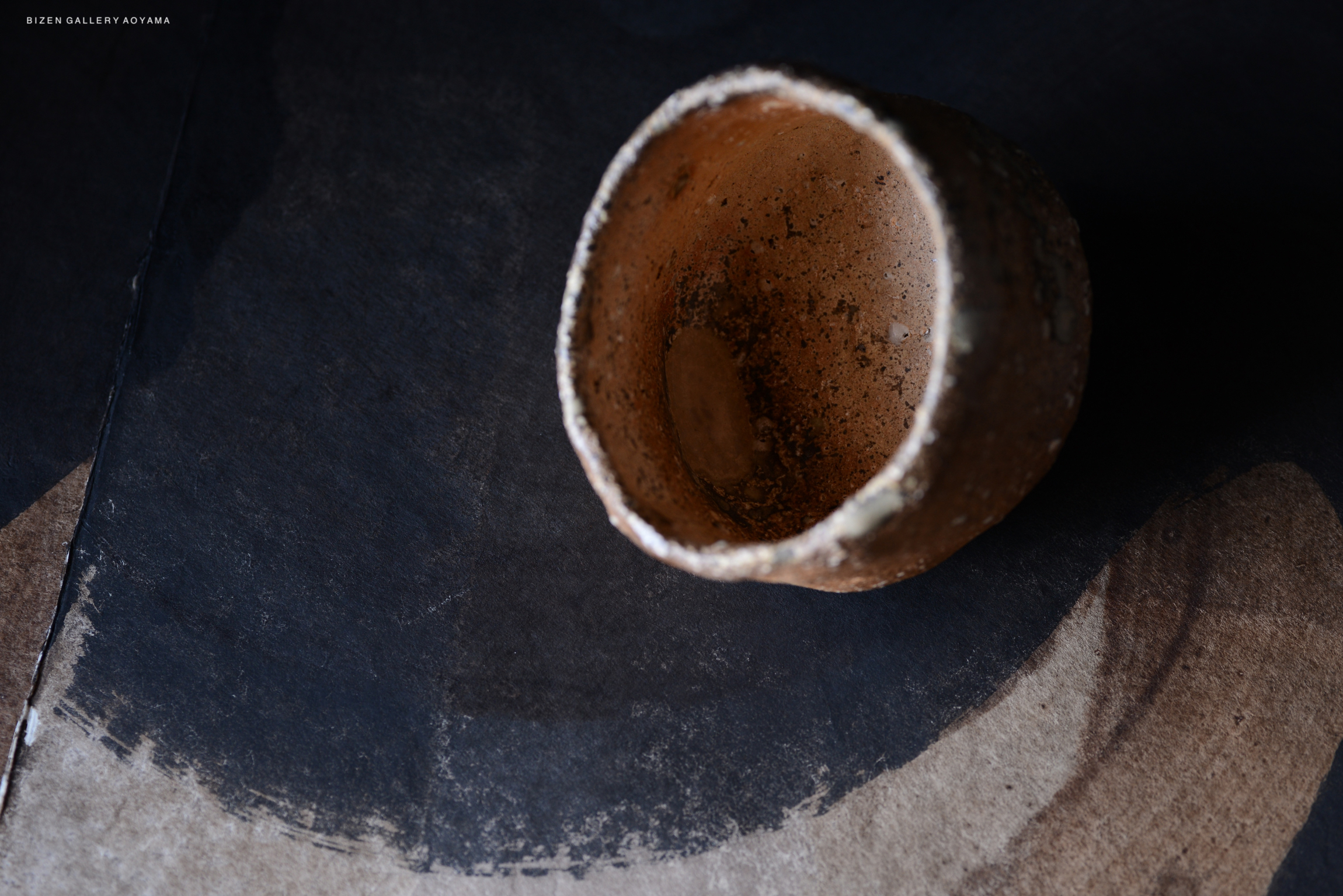 黒い背景の上に置かれた土器の画像。内側が見えるように撮影された古い土器で、周りには影とテクスチャーがある。