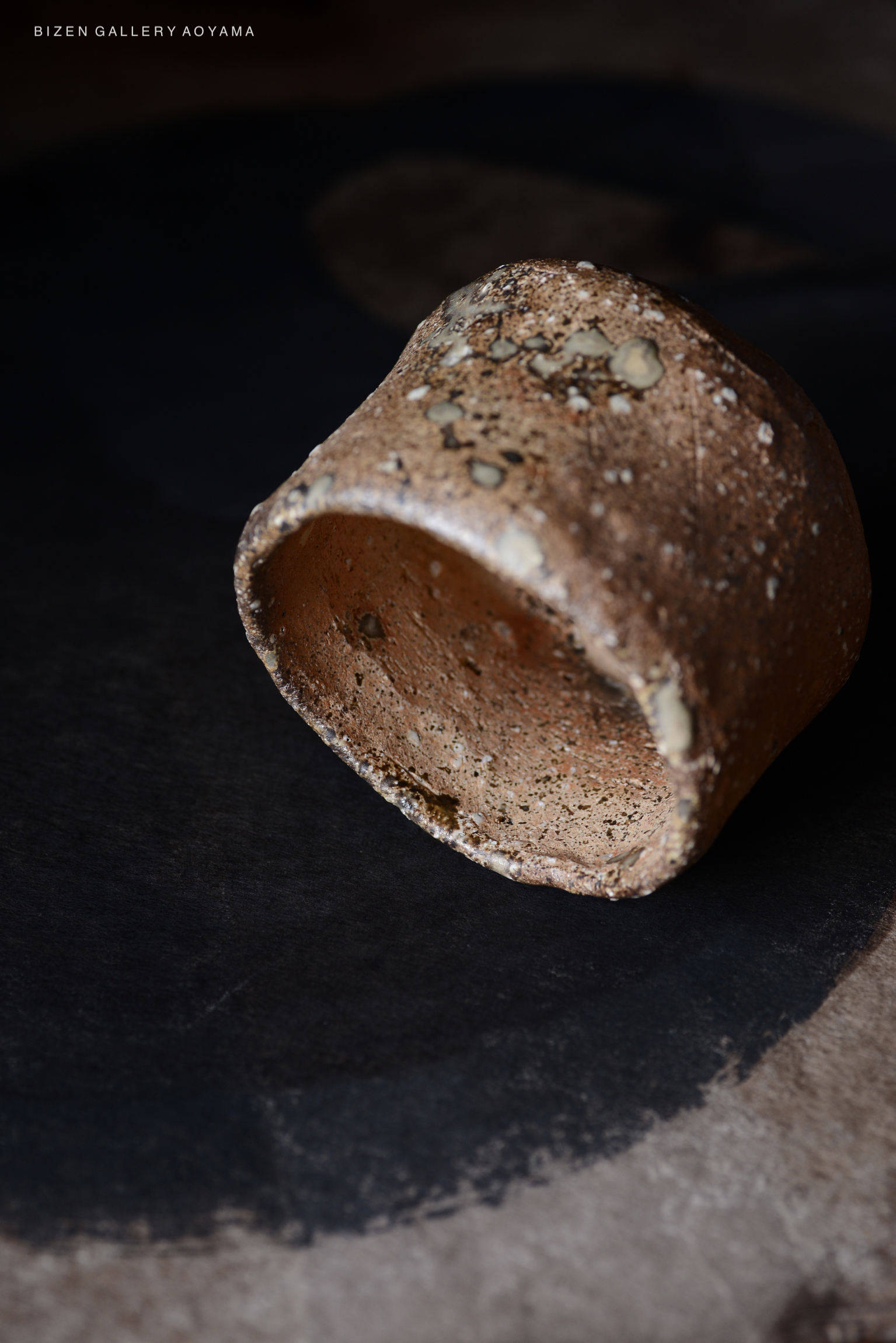 黒い背景の上に置かれた古い焼き物の陶器。表面には質感と自然な色合いが見られる。