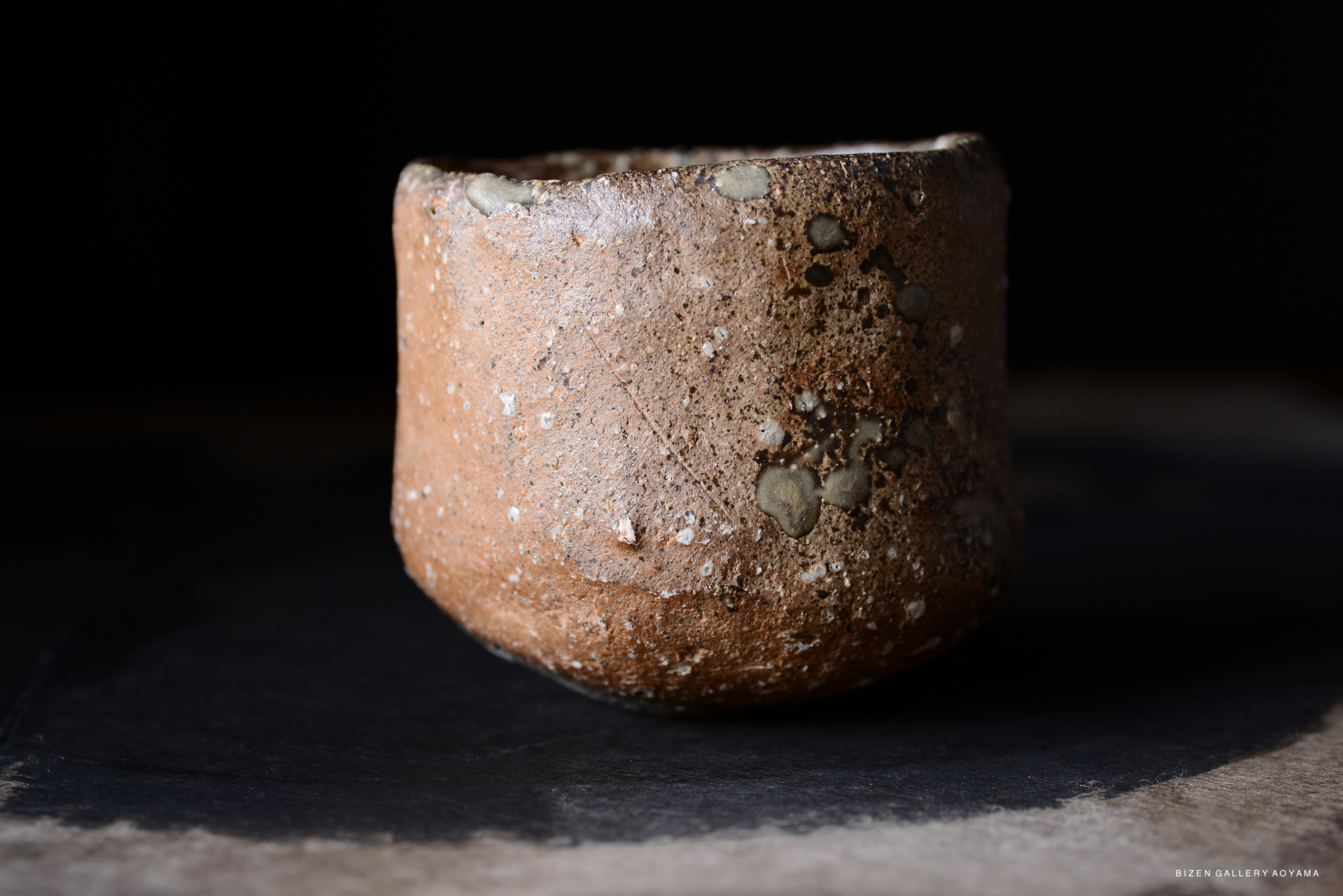 黒い背景の前に置かれた、質感のある土製の器の画像。