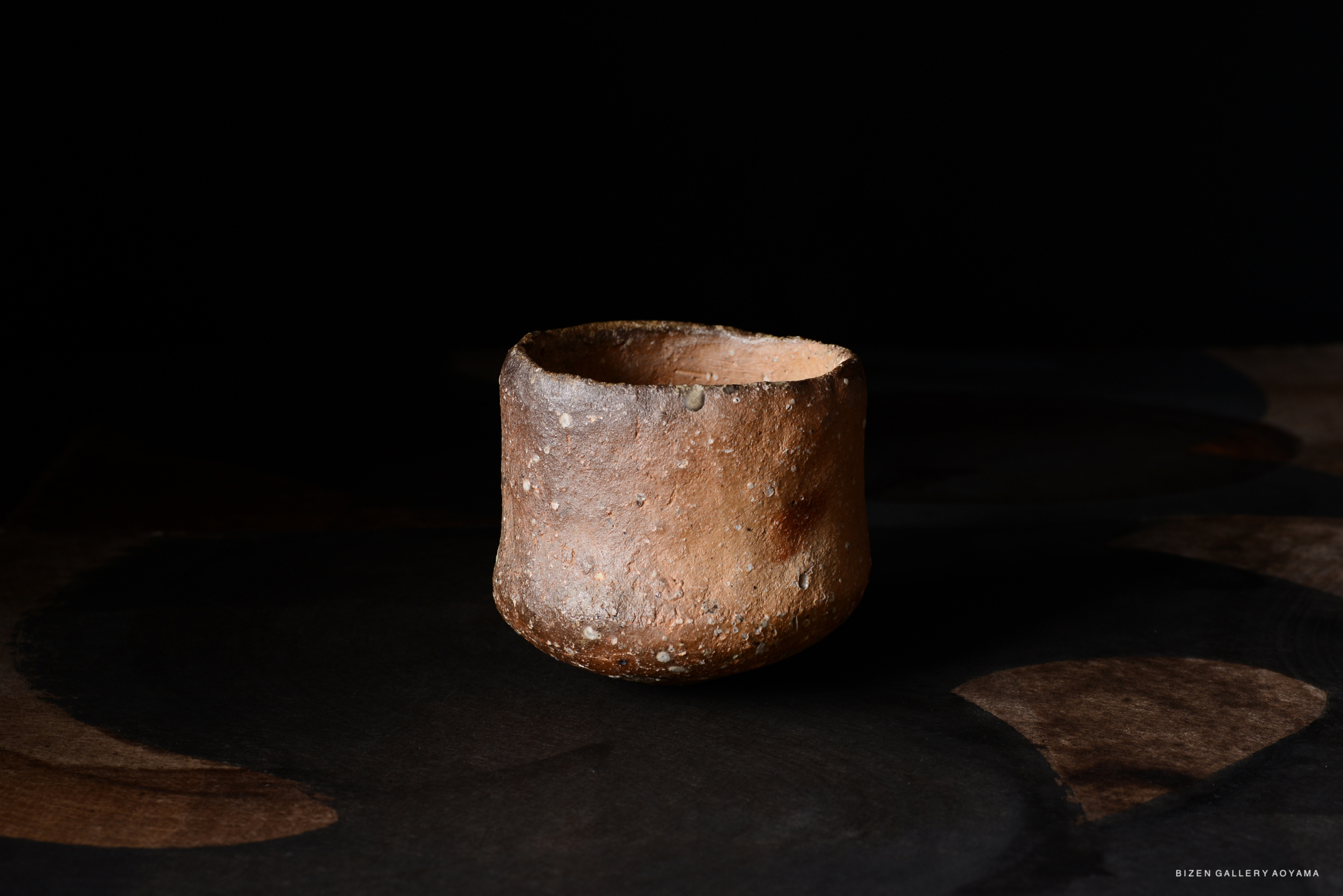 黒い背景の上に置かれた、土でできた素朴な陶器の器。