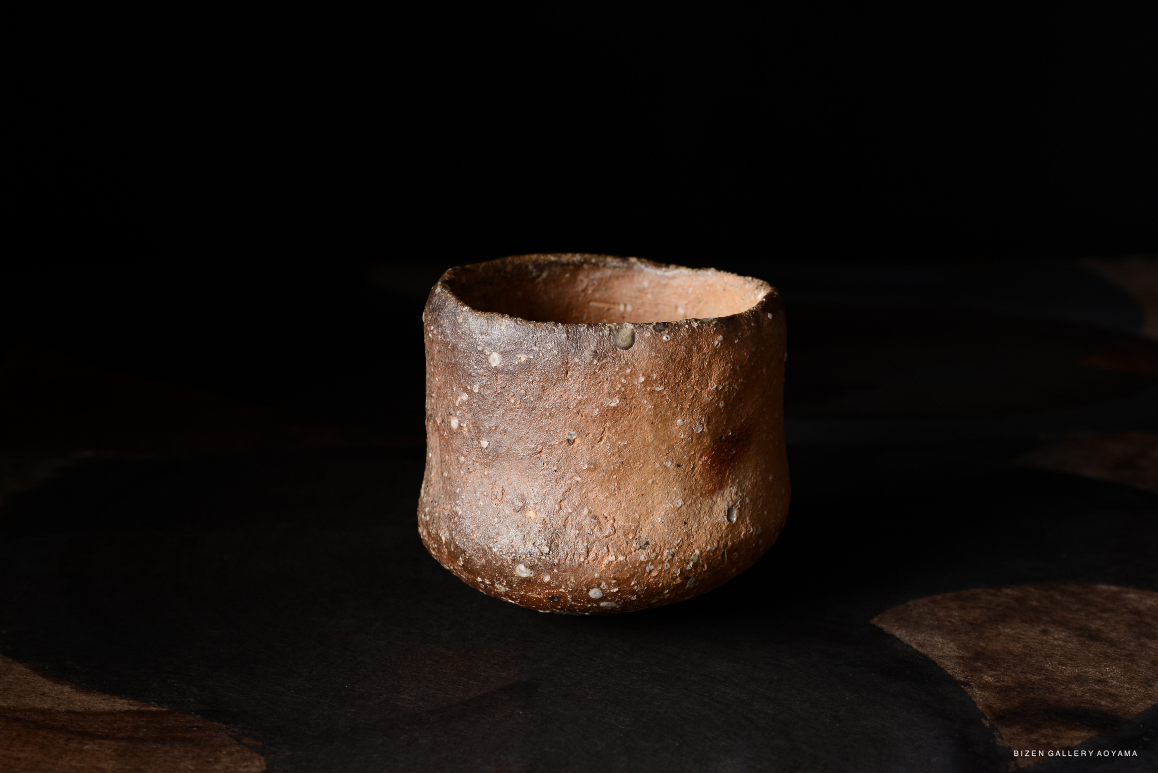 黒い背景に置かれた土製の茶碗。 textured な表面と独特な形状を持つ。