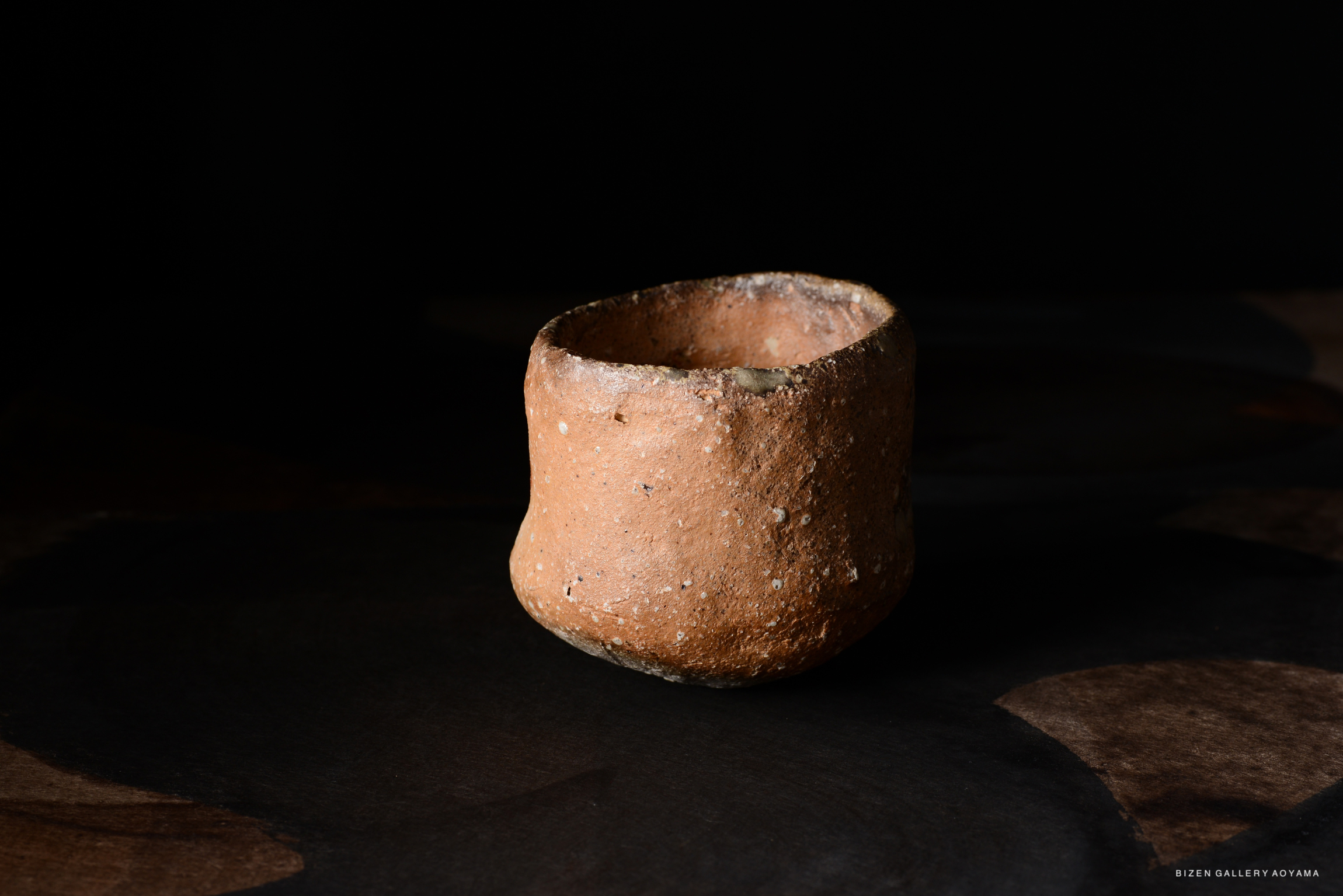 暗い背景に置かれた、素朴な陶製の器の写真。