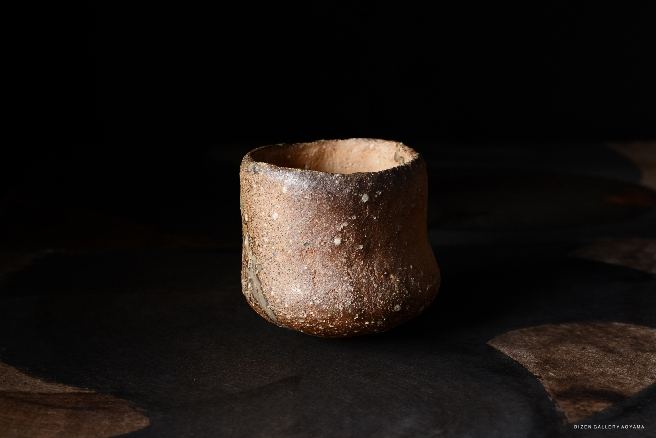 土器の上品な近接ショット、暗い背景に置かれた素朴な質感と色合いが特徴。