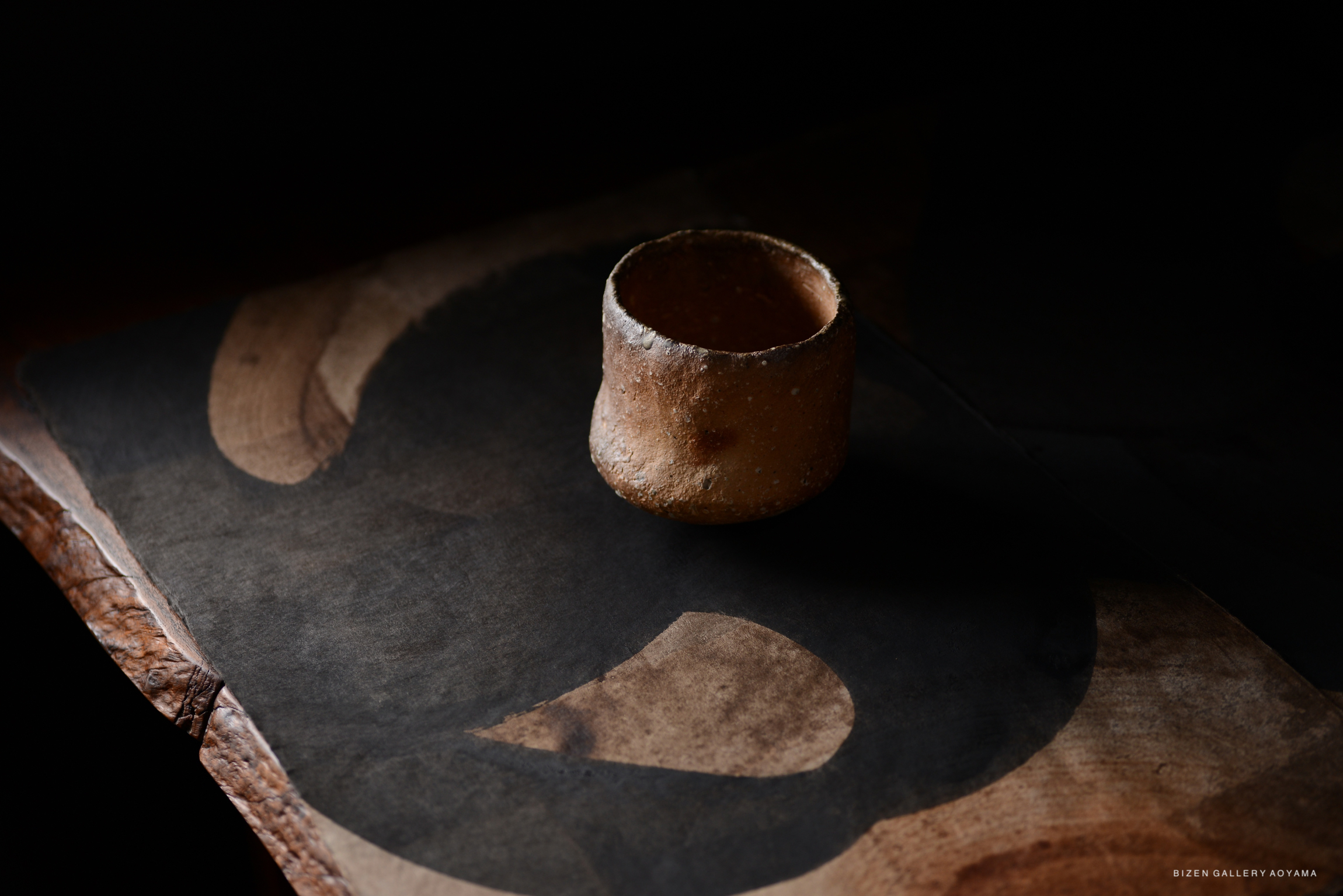 黒い背景の上に置かれた素朴な陶器のカップと抽象的な形状の紙