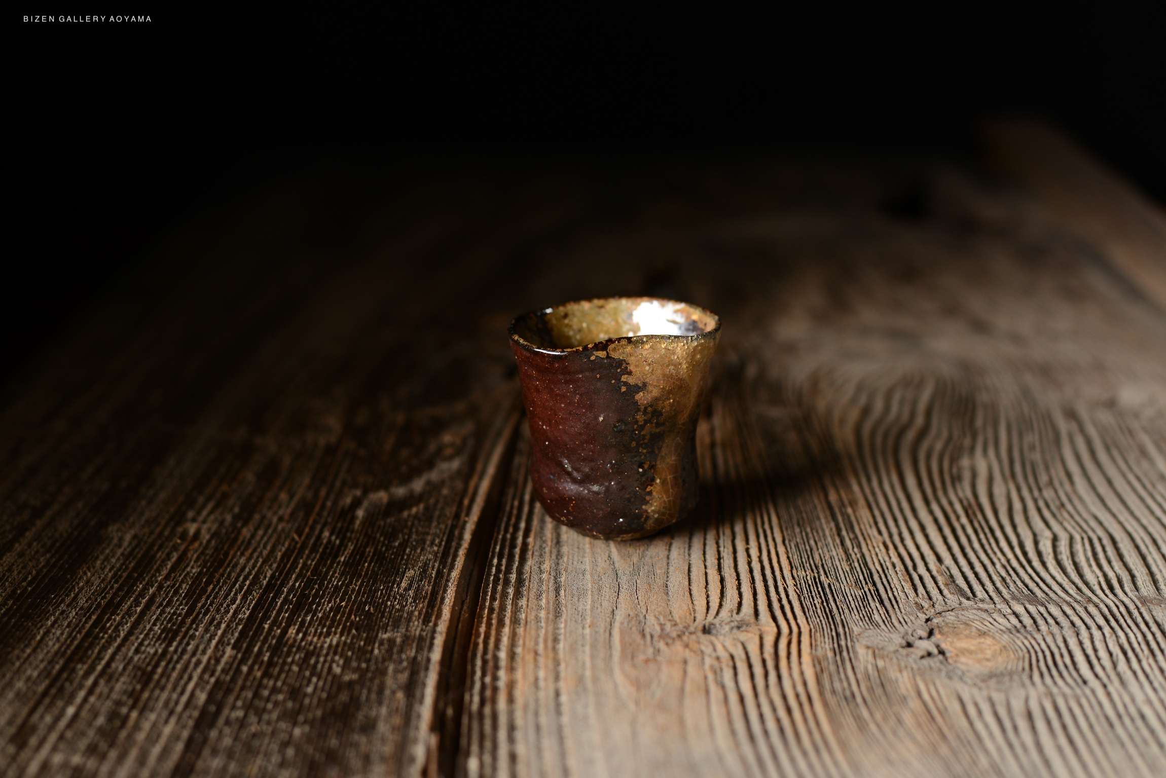 木製のテーブルの上に置かれた独特な形状の焼き物の器。肌色の外側と金色の内側が特徴的。