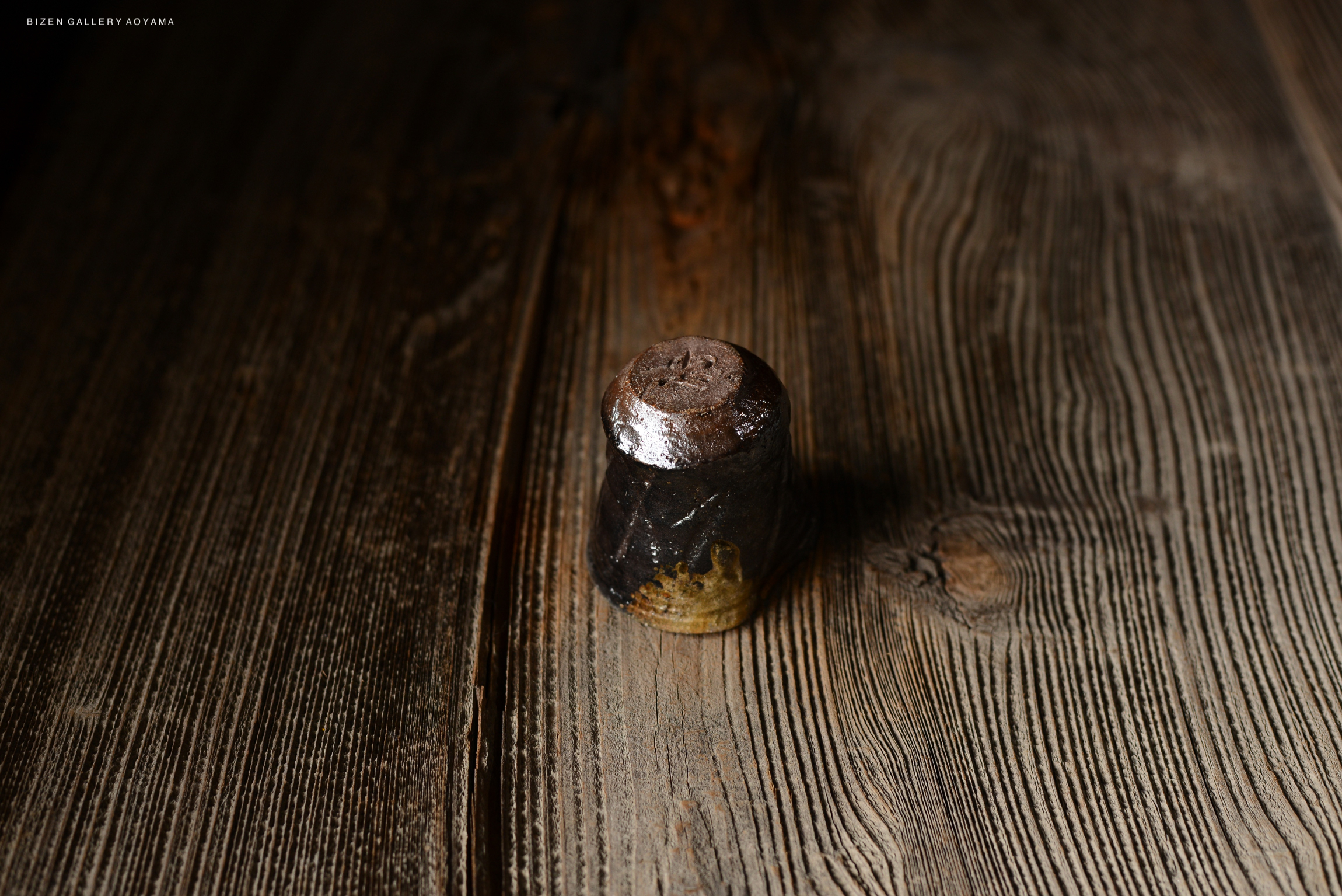 木製テーブルの上に置かれた陶磁器の小さな器。表面は光沢があり、下部は自然な質感を持っている。