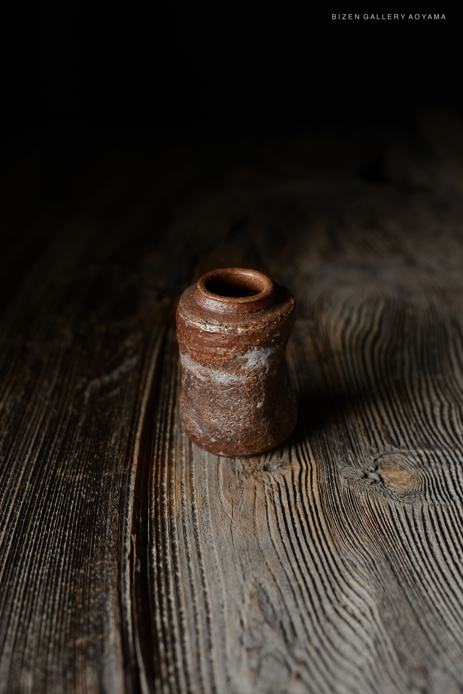 暗い背景の上に置かれた、陶器製の小さな容器。木のテーブルの上で撮影されている。