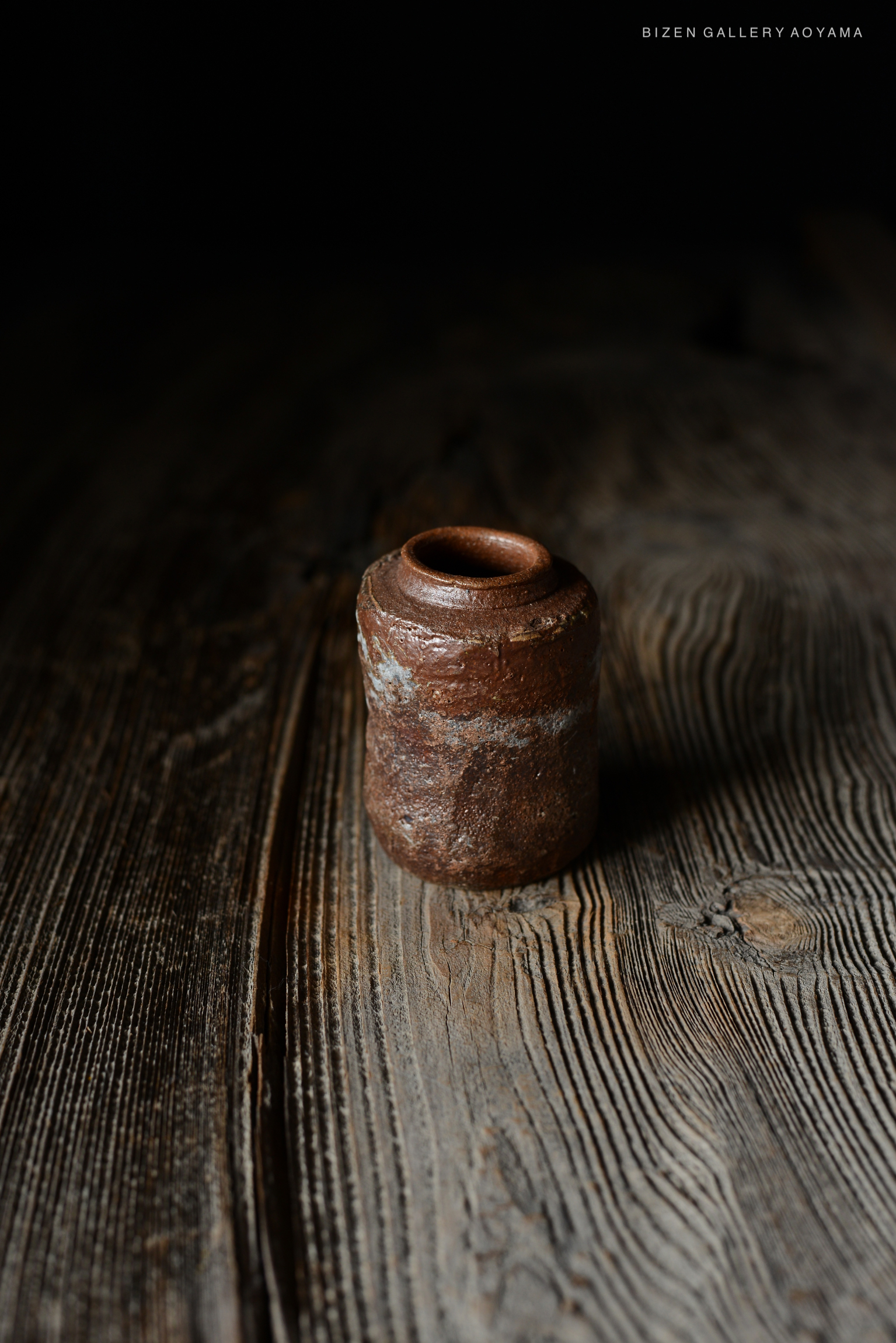 暗い背景に置かれた素朴な茶色の陶器の壺を上から見た写真。木製のテーブルの上に置かれている。