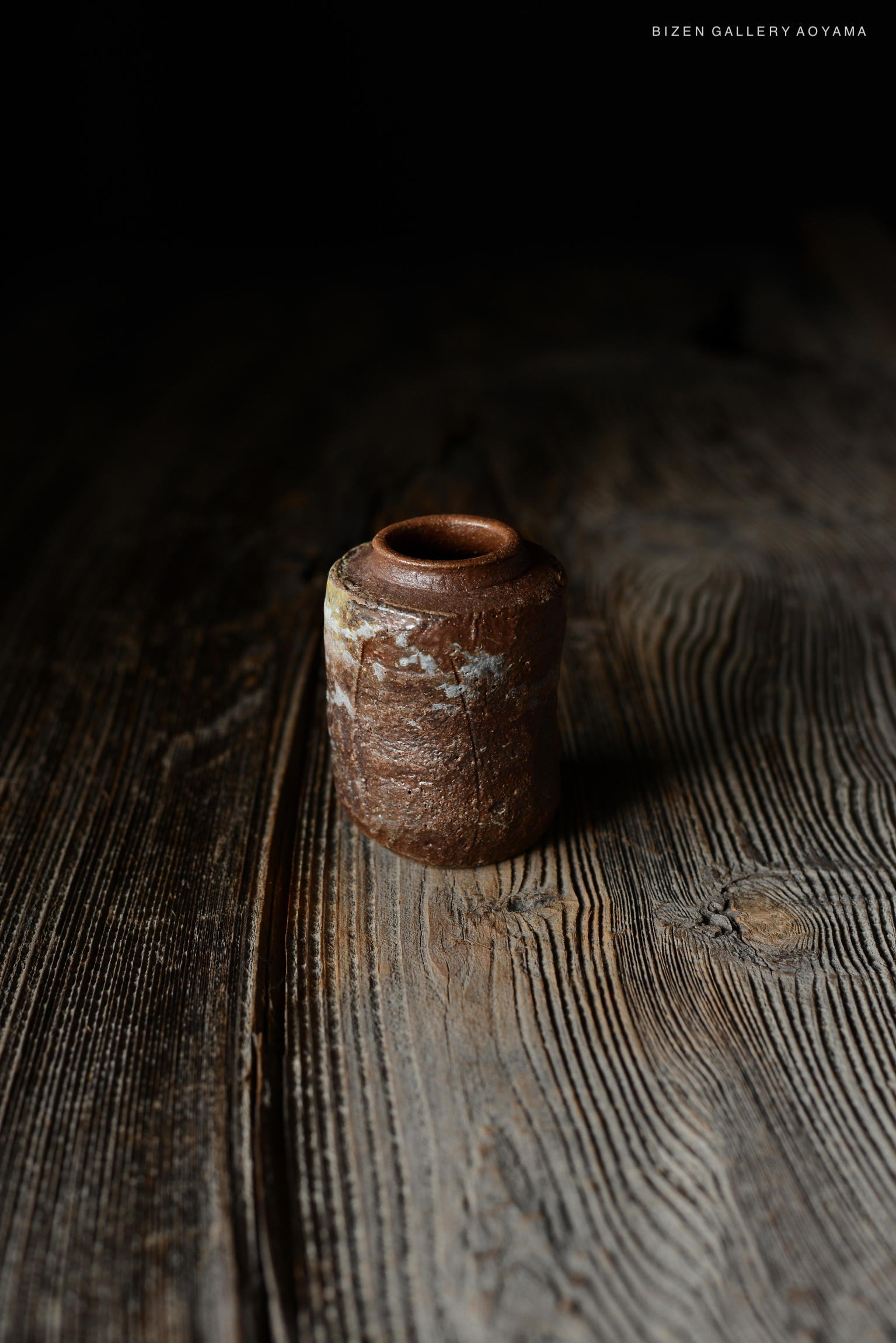 暗い背景の上に置かれた、和風の素焼きの壺がテーブルの上にある様子。