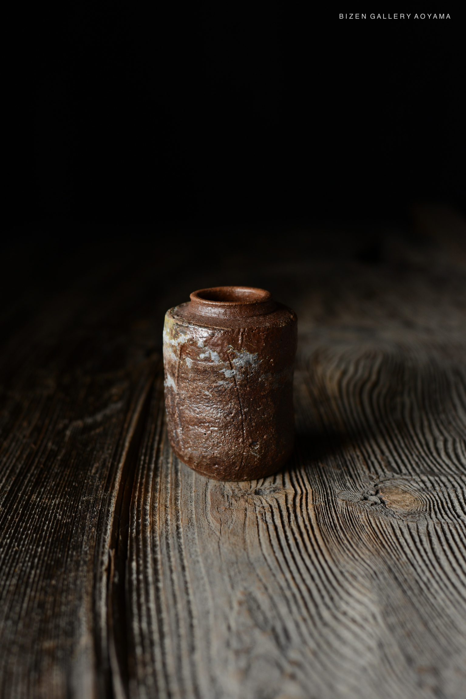 暗い背景の上に置かれたビゼン焼きの茶色い陶器の壺