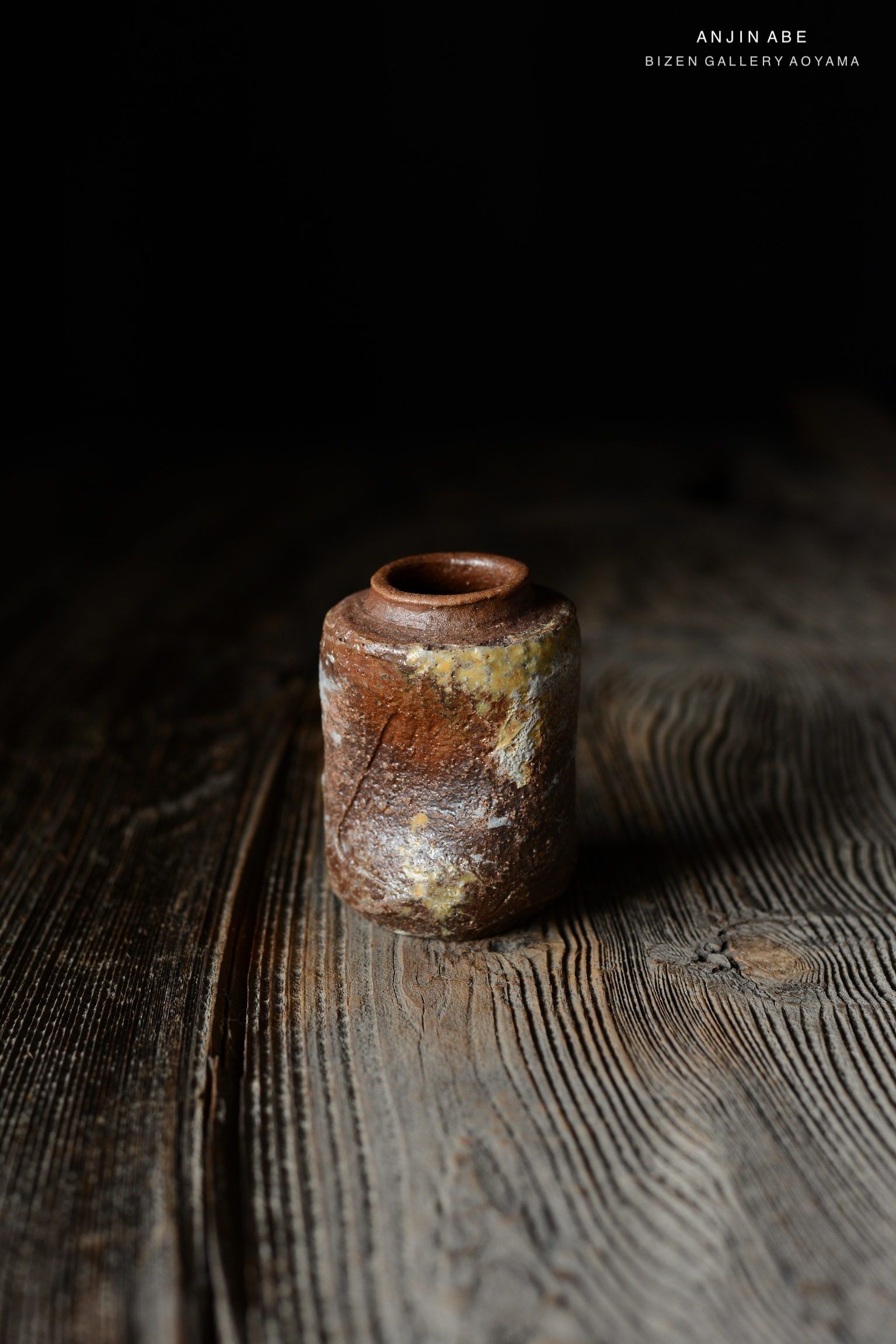 暗い背景の上に置かれたビゼン焼の陶器の花瓶。木のテーブルの上で、自然なテクスチャーが際立っている。