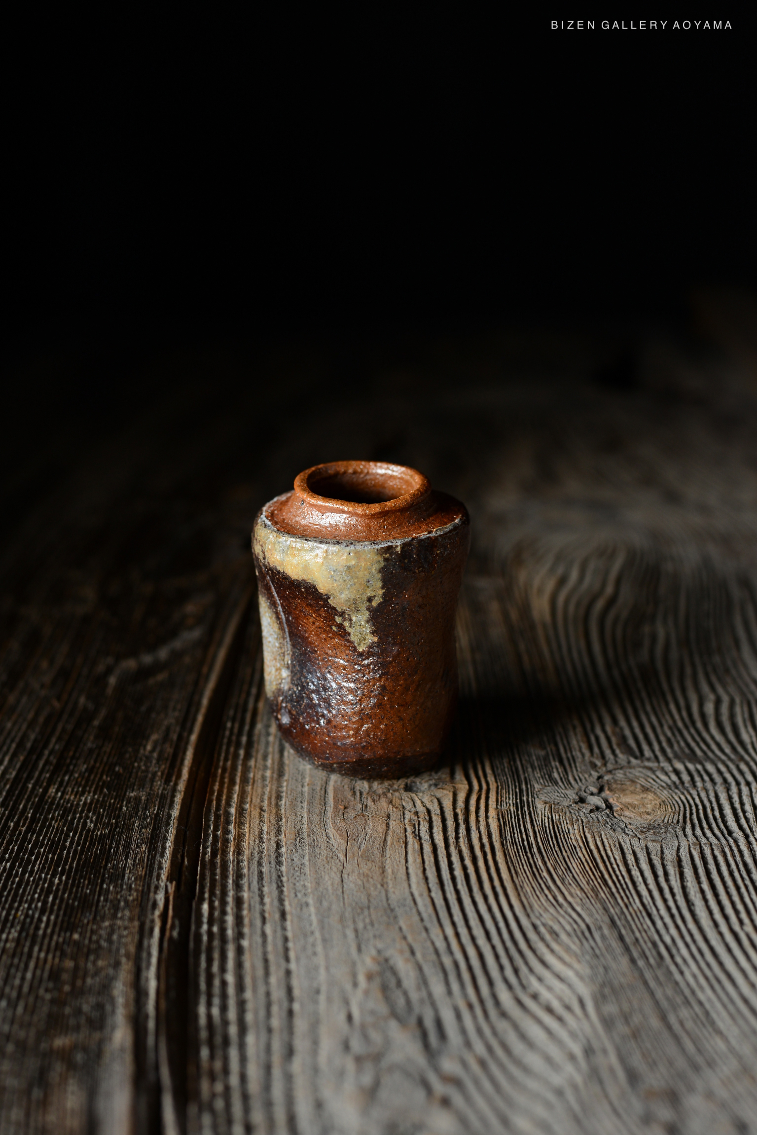 暗い背景に置かれた、独特な形状の備前焼の陶器。木のテーブルの上に置かれている。