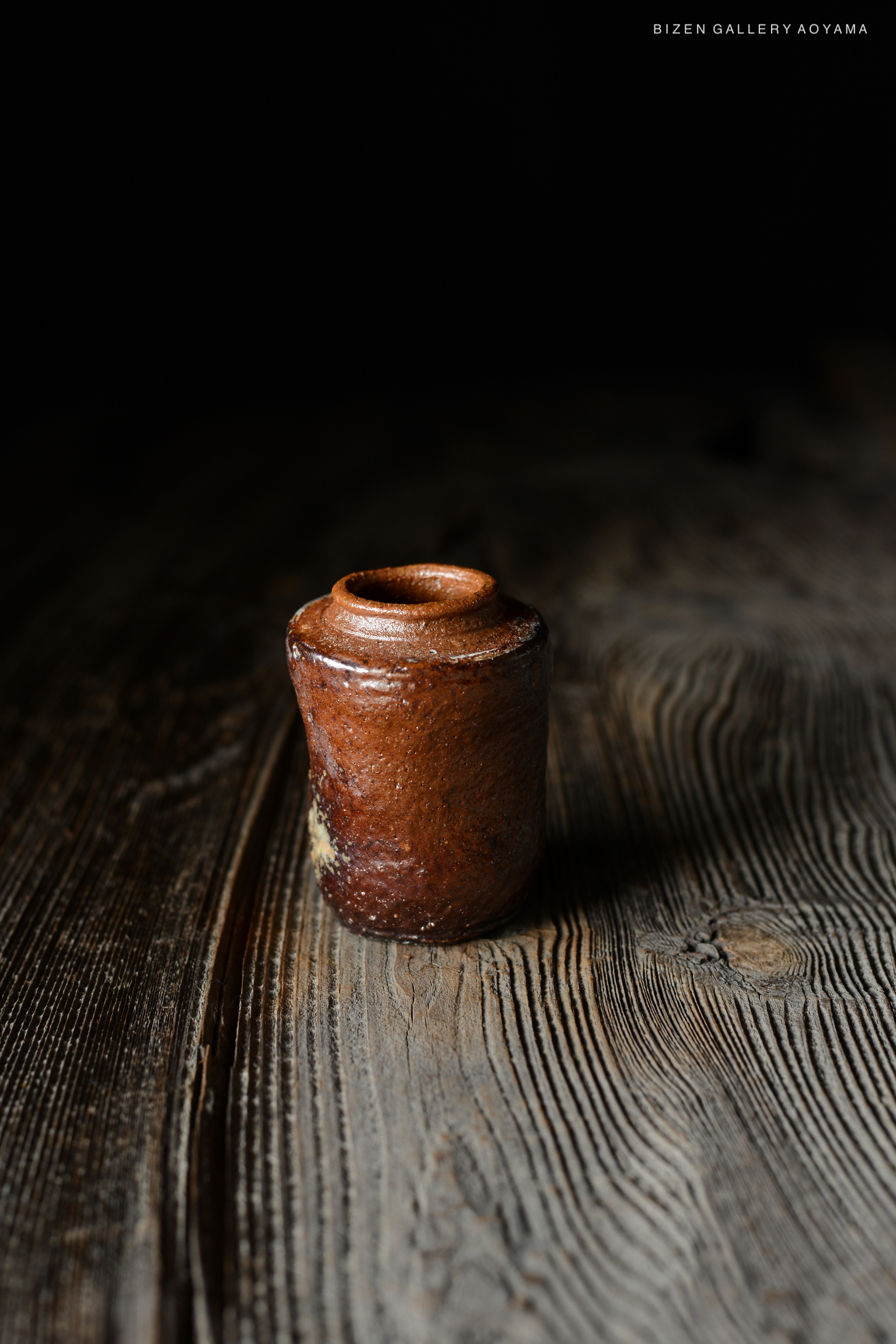 黒い背景の上に置かれた陶器の瓶。木製のテーブルの上にあり、自然な質感が目立つ。